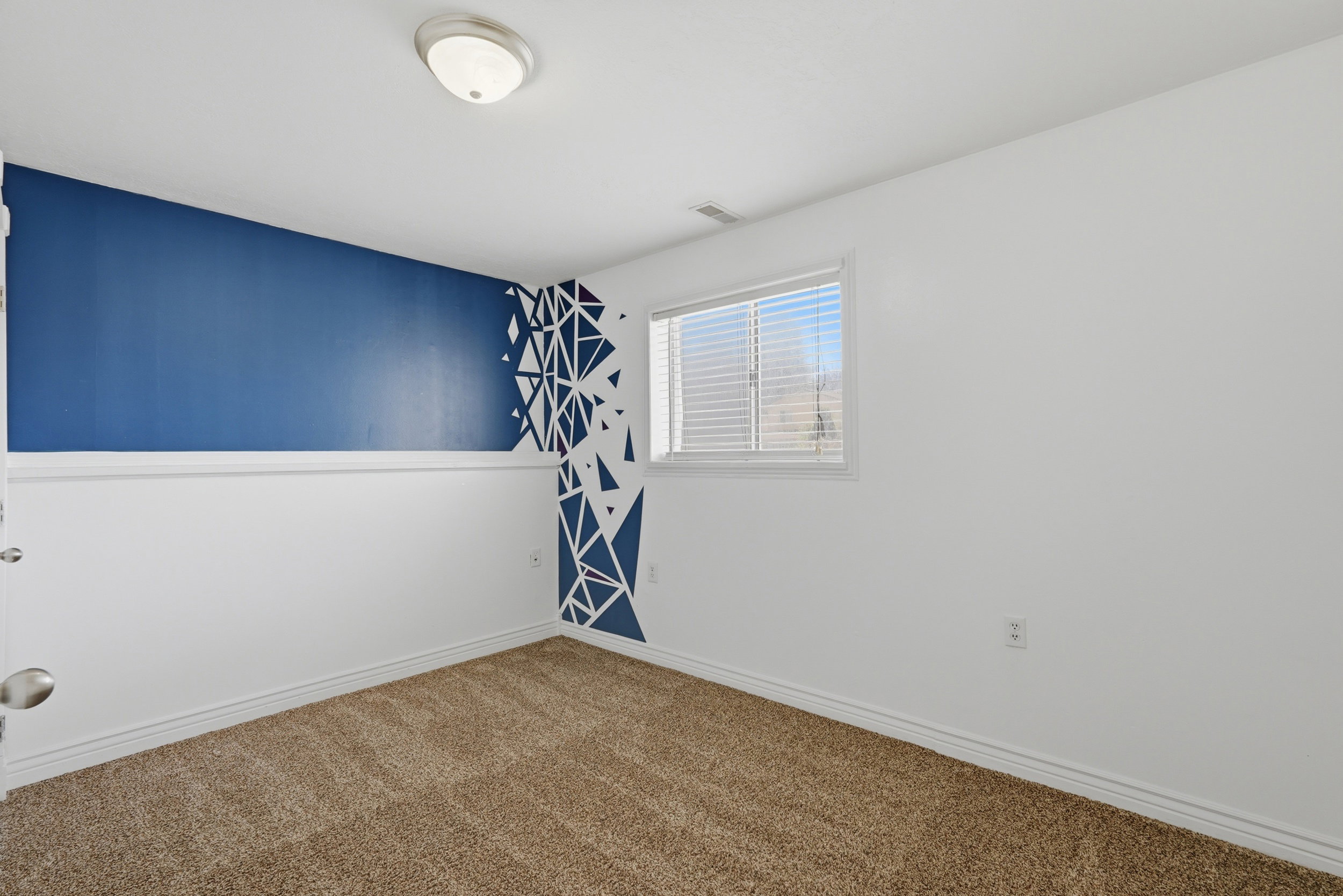 Room featuring neutral-toned carpet flooring, white baseboards, and a contrasting blue accent wall with a geometric pattern