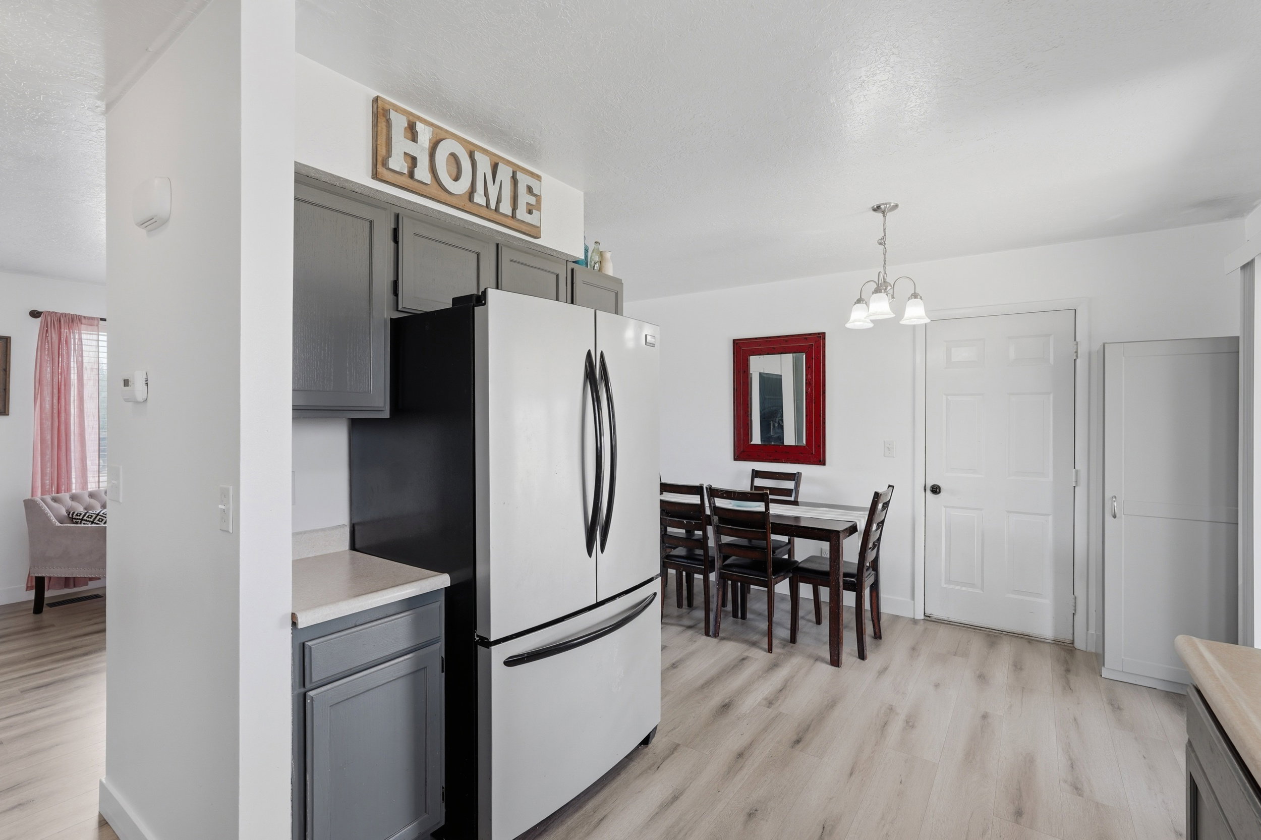 Kitchen and dining area featuring light wood-finish flooring, grey cabinetry with light countertops, a built-in refrigerator, and a dining table with chairs