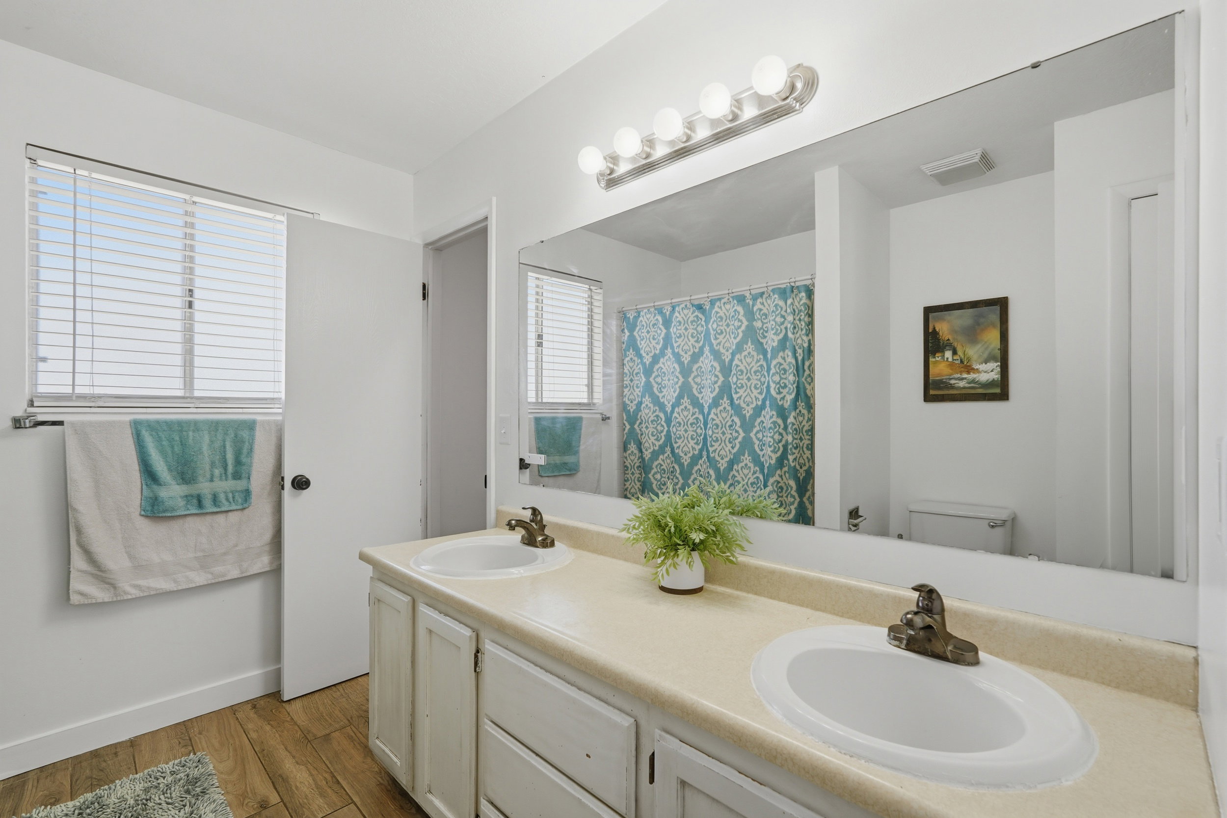 Bathroom featuring a double vanity with integrated sinks, a large wall-mounted mirror, and wood-finish flooring