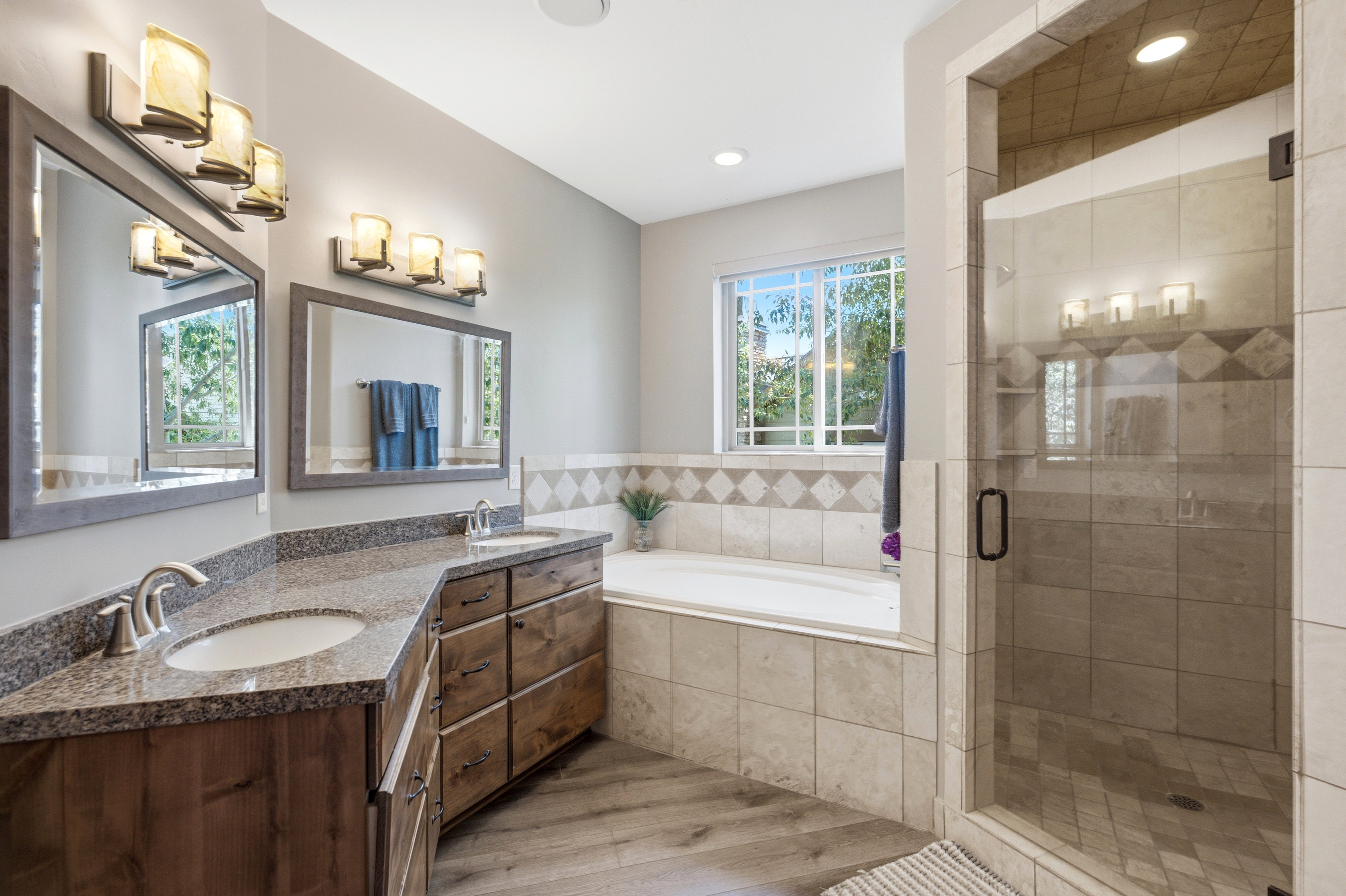 Bathroom featuring a glass-enclosed shower, a deep soaking tub, and a double vanity with stone countertops