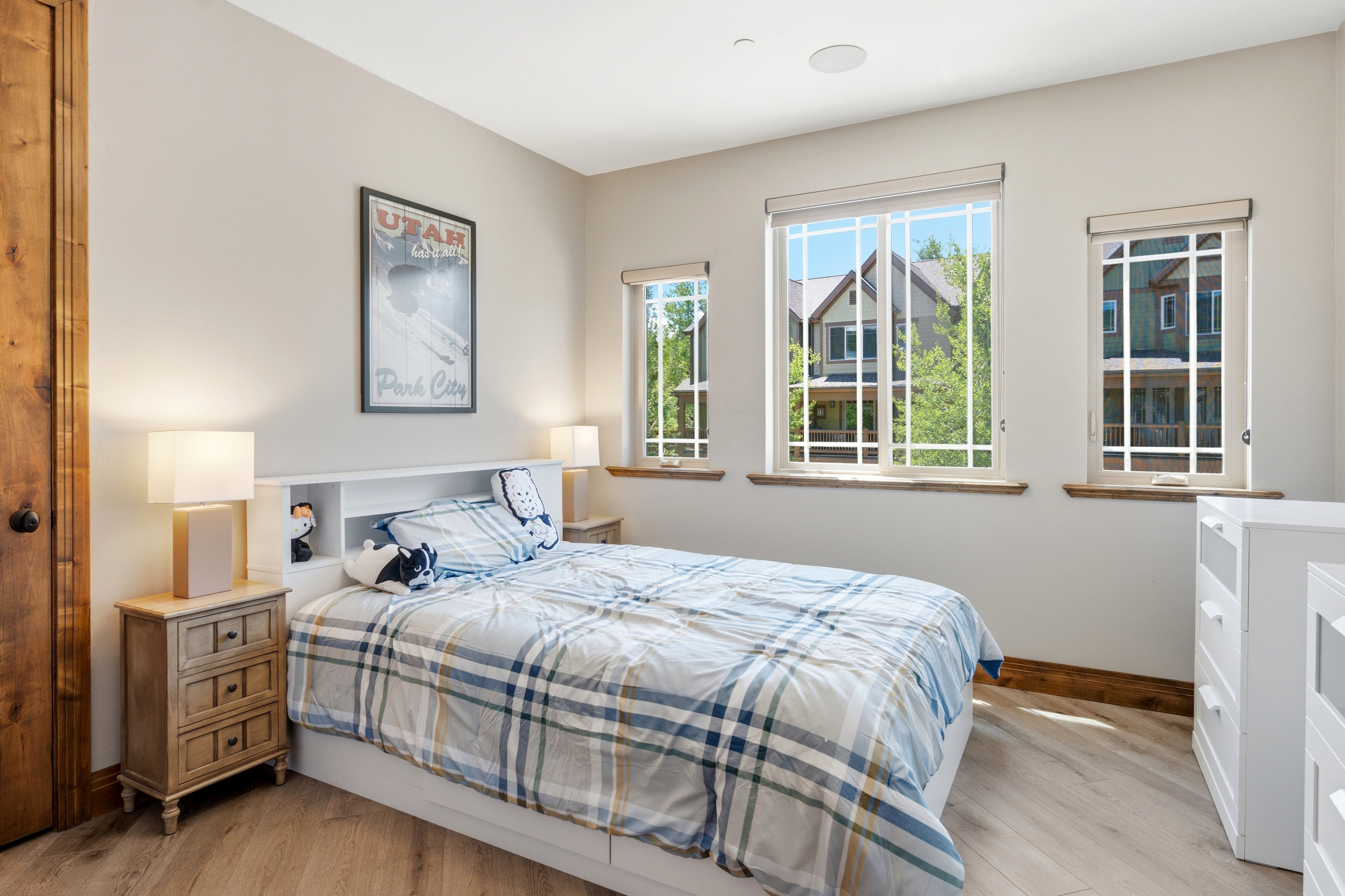 Room featuring multiple windows with grid patterns, wood-finish flooring, and a built-in headboard with integrated shelving