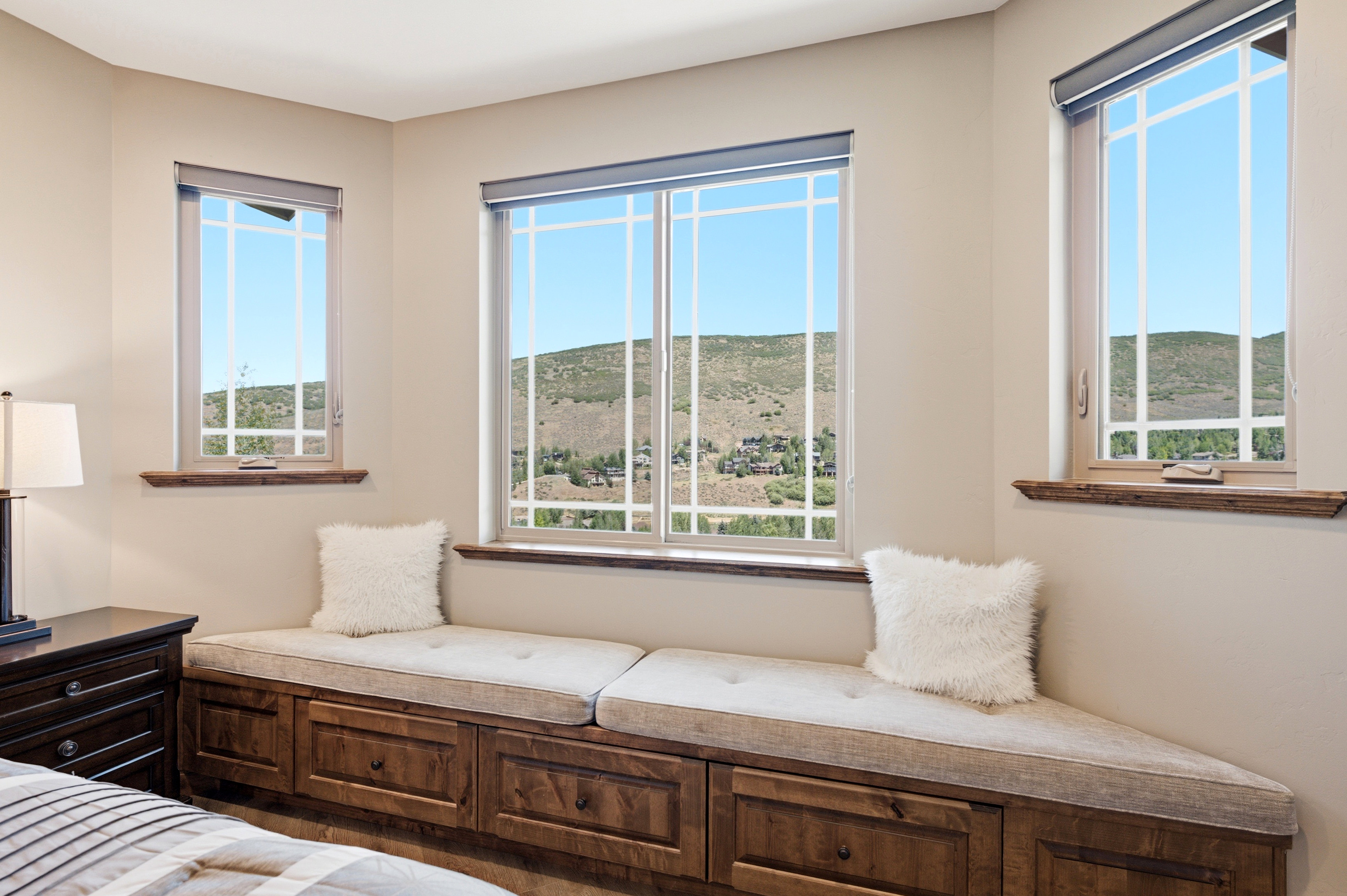 Corner window seat with built-in storage drawers, featuring three individual windows with grilles