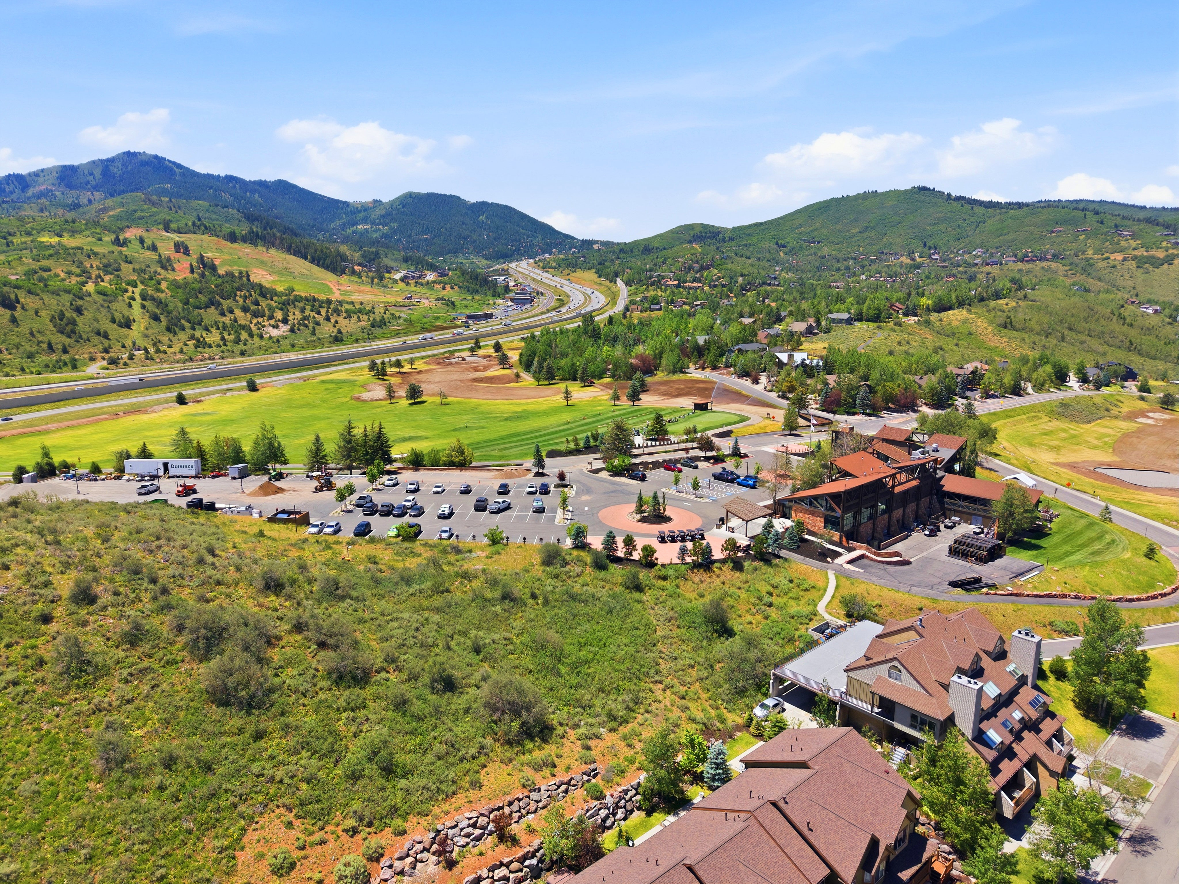 Expansive mountain landscape featuring a multi-lane highway, green fields, and a commercial building with a circular driveway