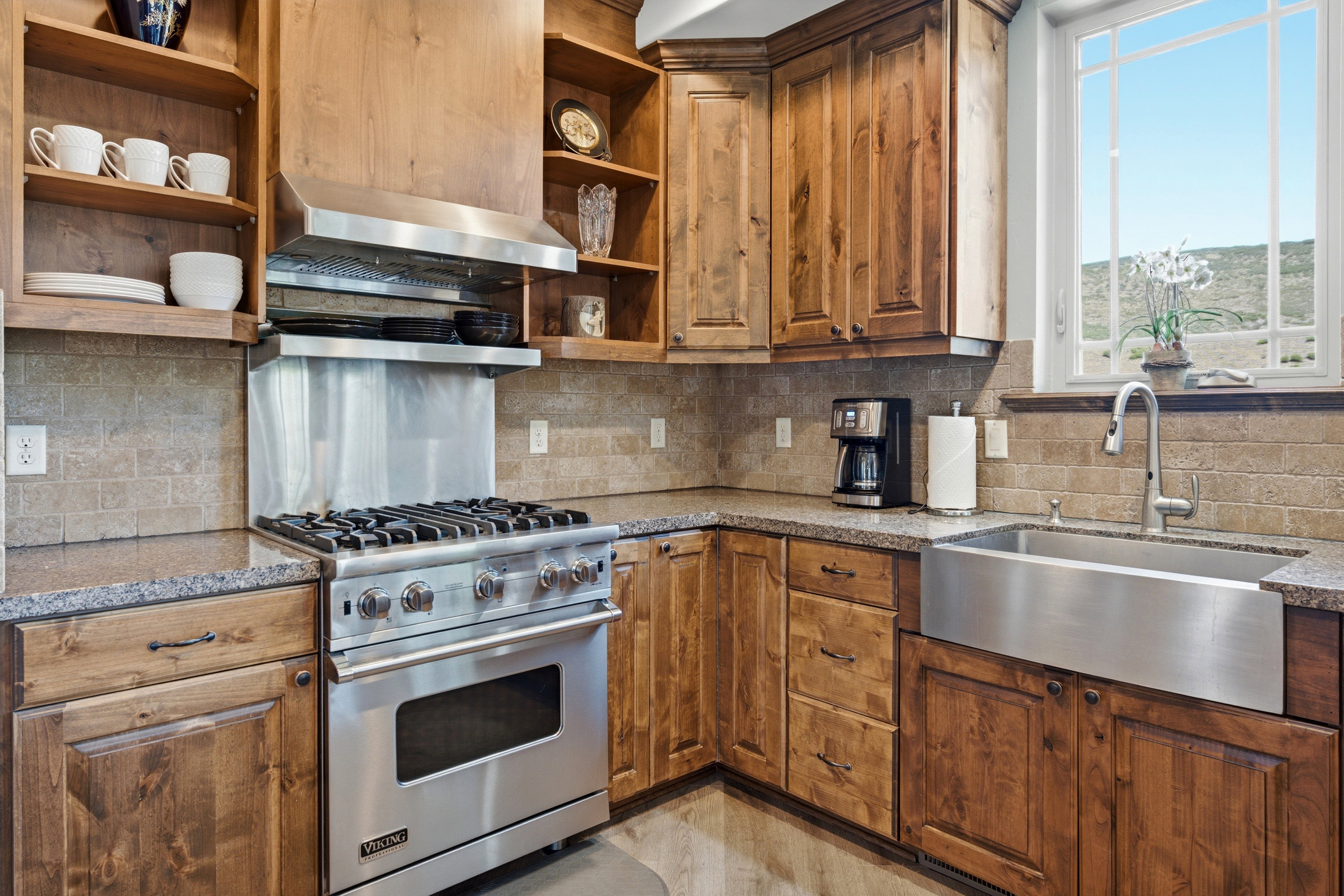 Gourmet kitchen featuring a stainless steel Viking range with hood, natural wood cabinetry, stone countertops, and a stainless steel farmhouse sink