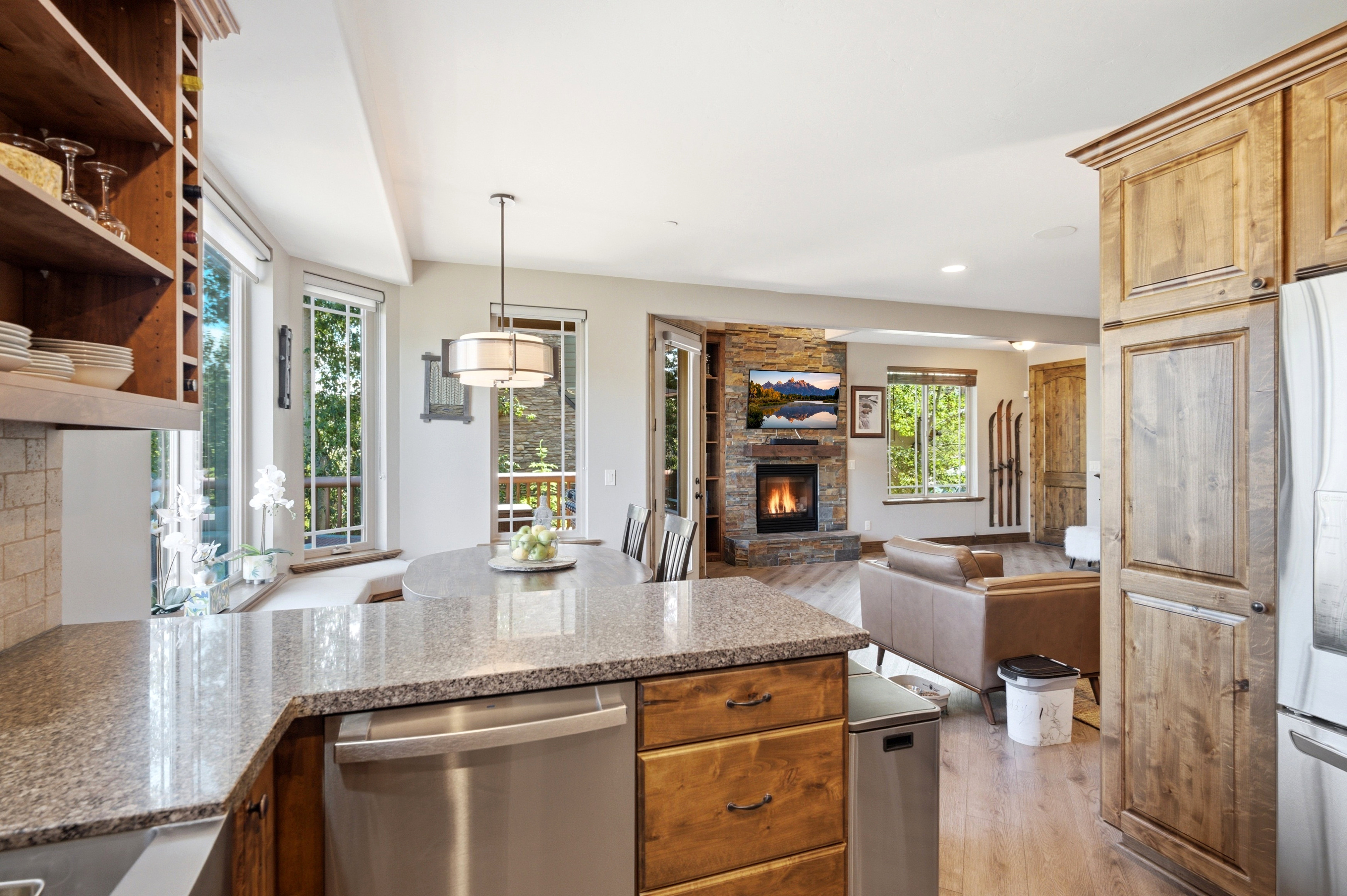 Kitchen featuring granite countertops, wood-finish flooring, custom wood cabinetry, stainless steel dishwasher, and a stone-clad fireplace