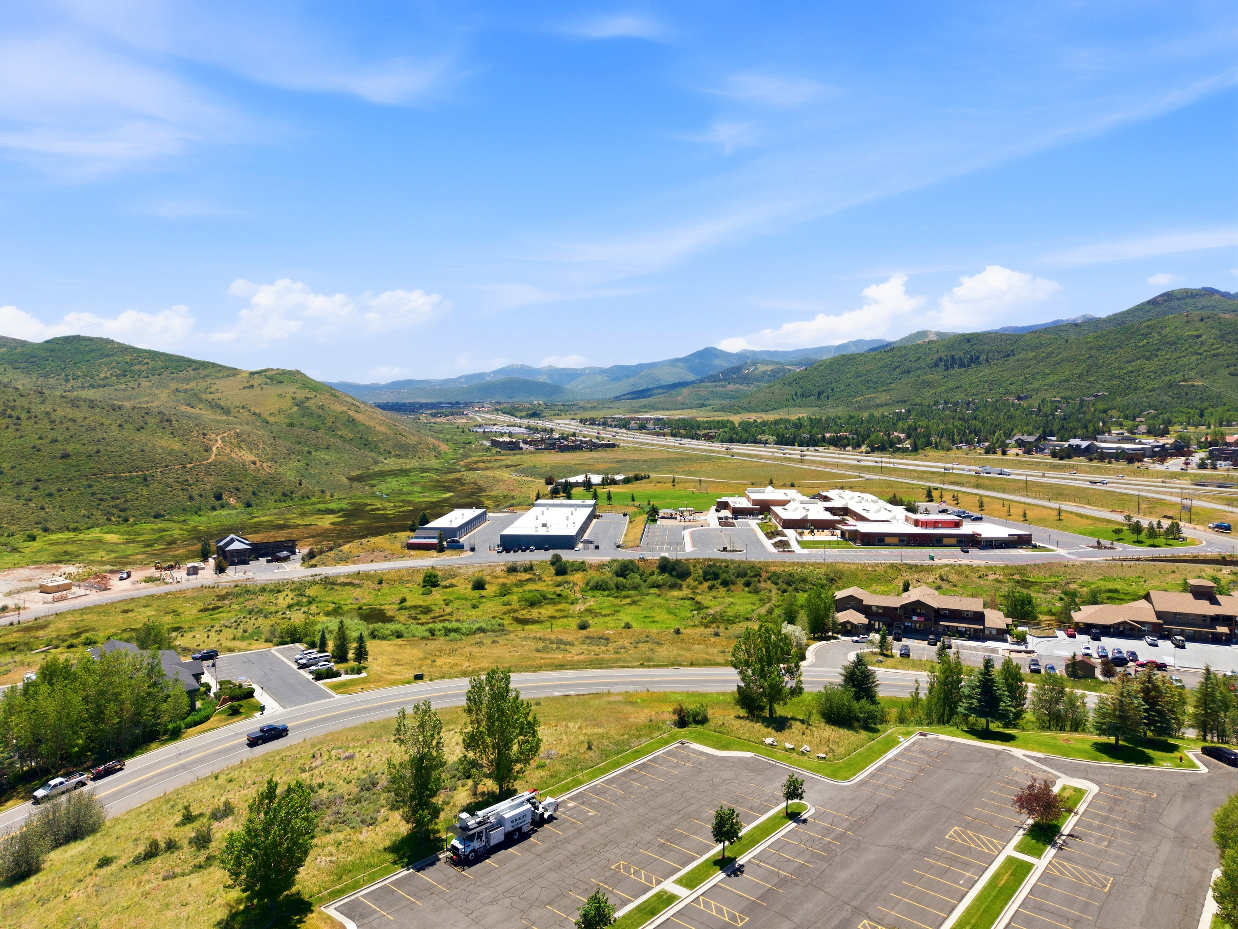 Expansive mountainous landscape featuring multiple commercial buildings with paved parking areas and a multi-lane highway