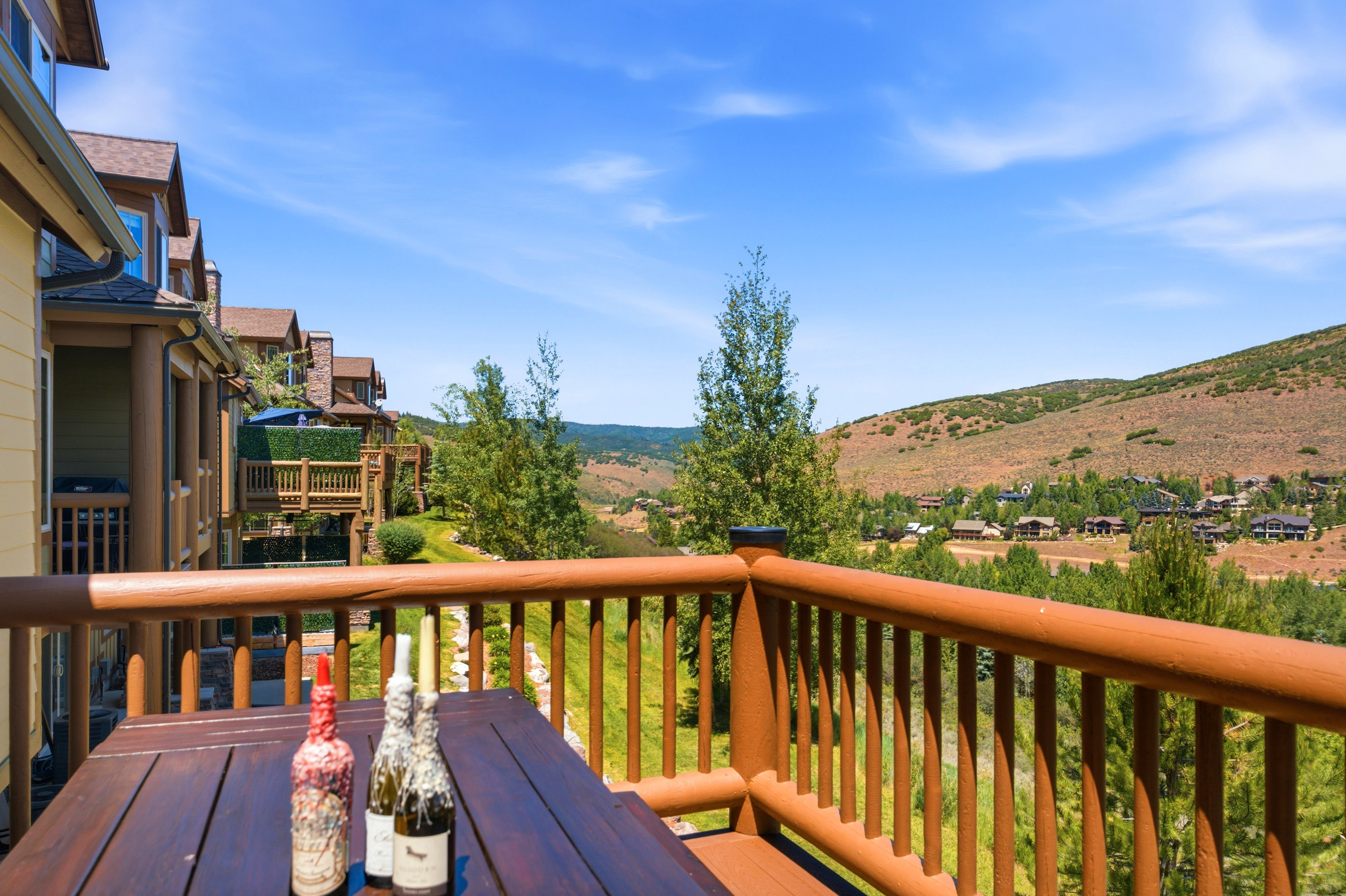 Outdoor deck with wood railings and a wood-finish table, overlooking a hillside community