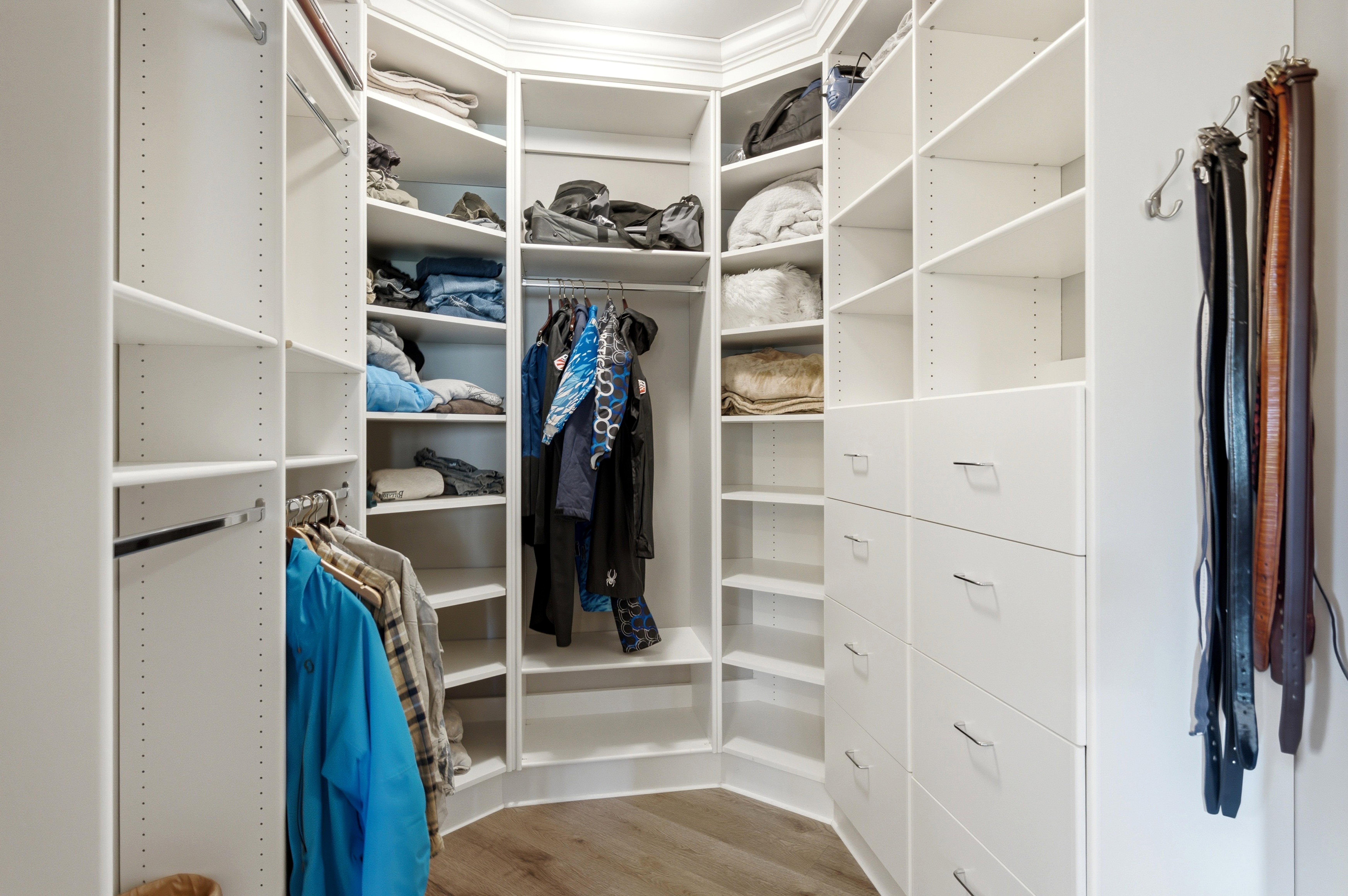 Custom-designed walk-in closet featuring extensive white shelving, multiple hanging rods, built-in drawers with polished hardware, and wood-finish flooring