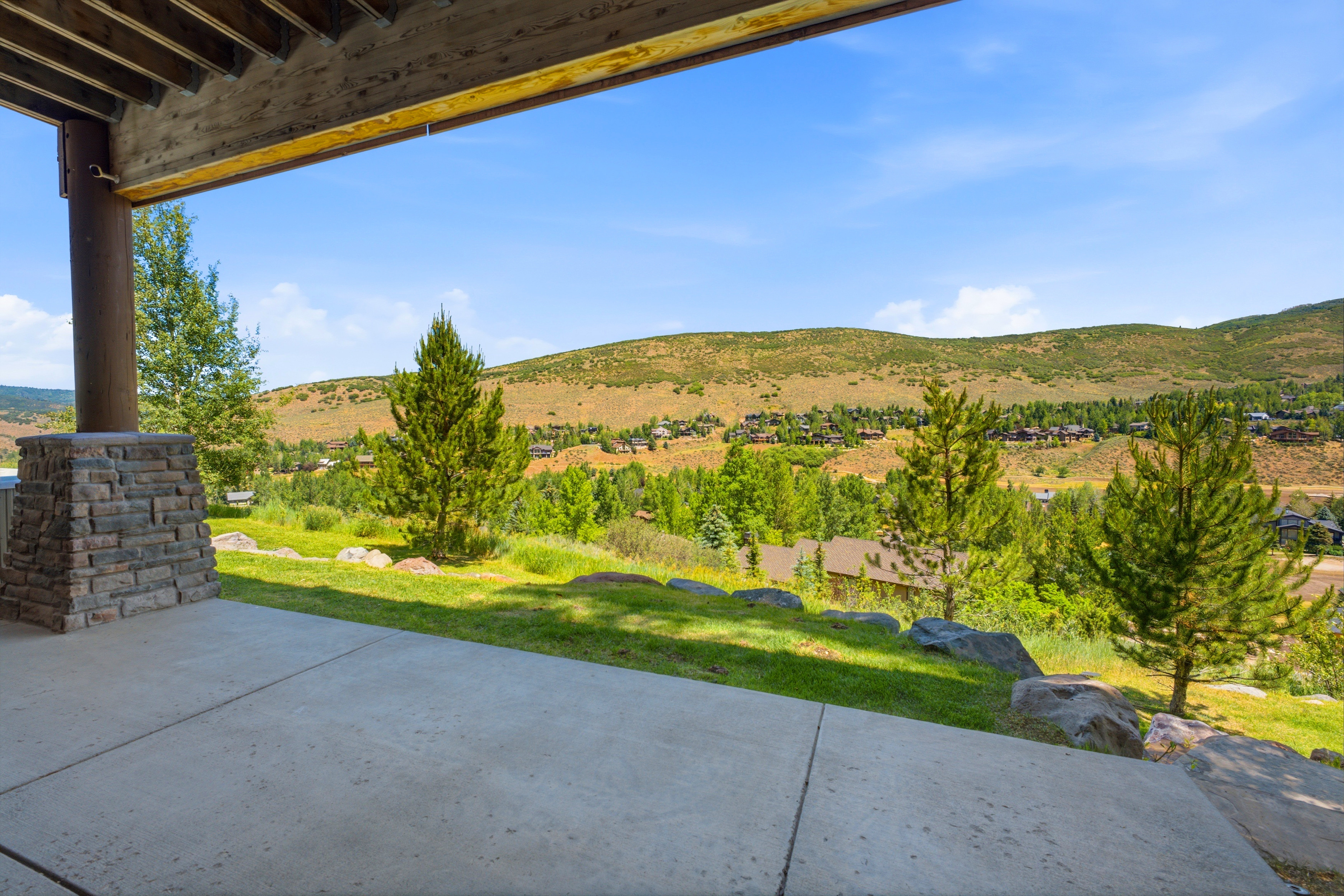 Expansive concrete patio with a stacked stone column, featuring a natural landscape with mature trees and distant residential structures