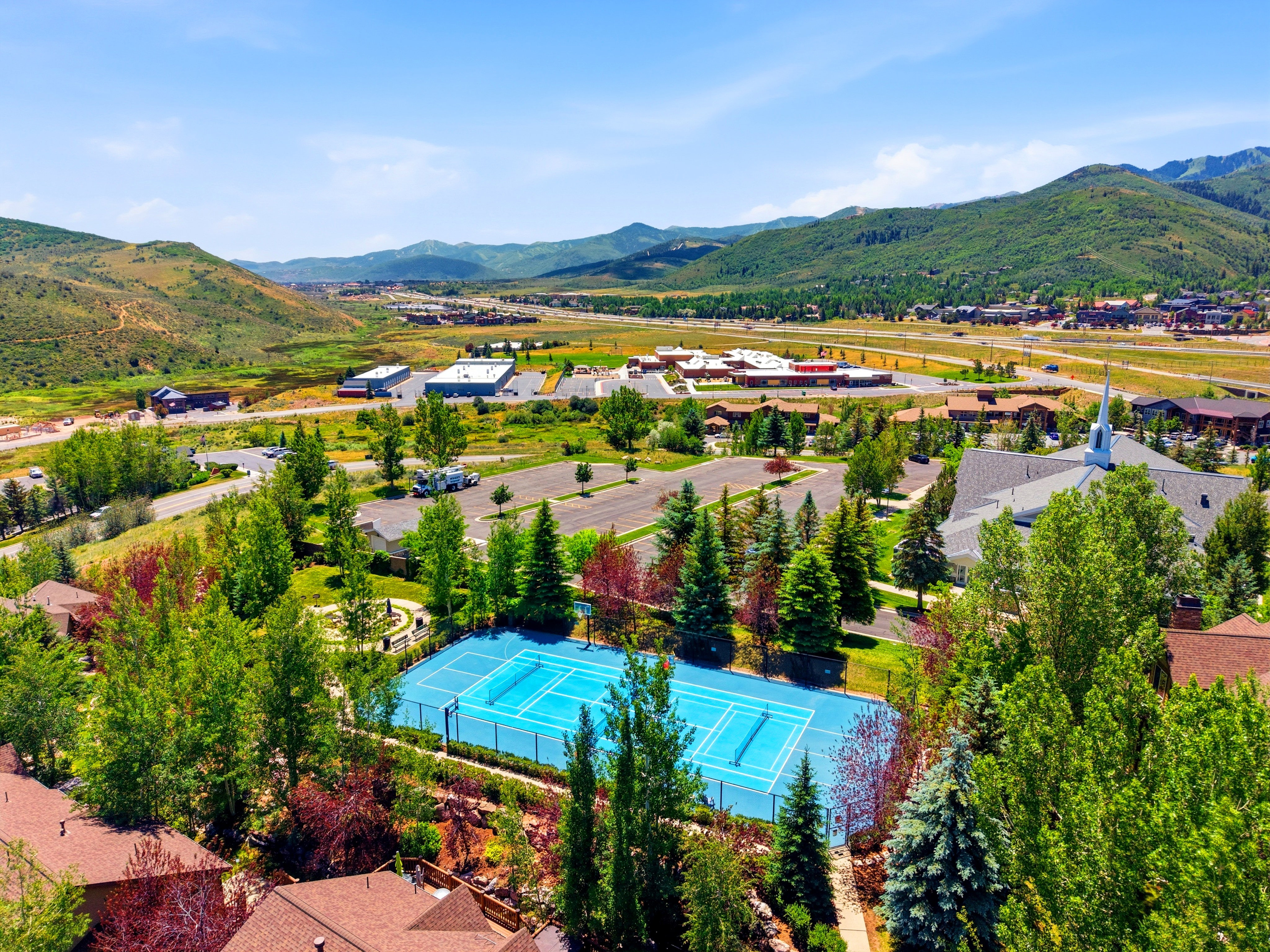 Outdoor tennis court with a bright blue playing surface, surrounded by mature trees and lush green landscaping