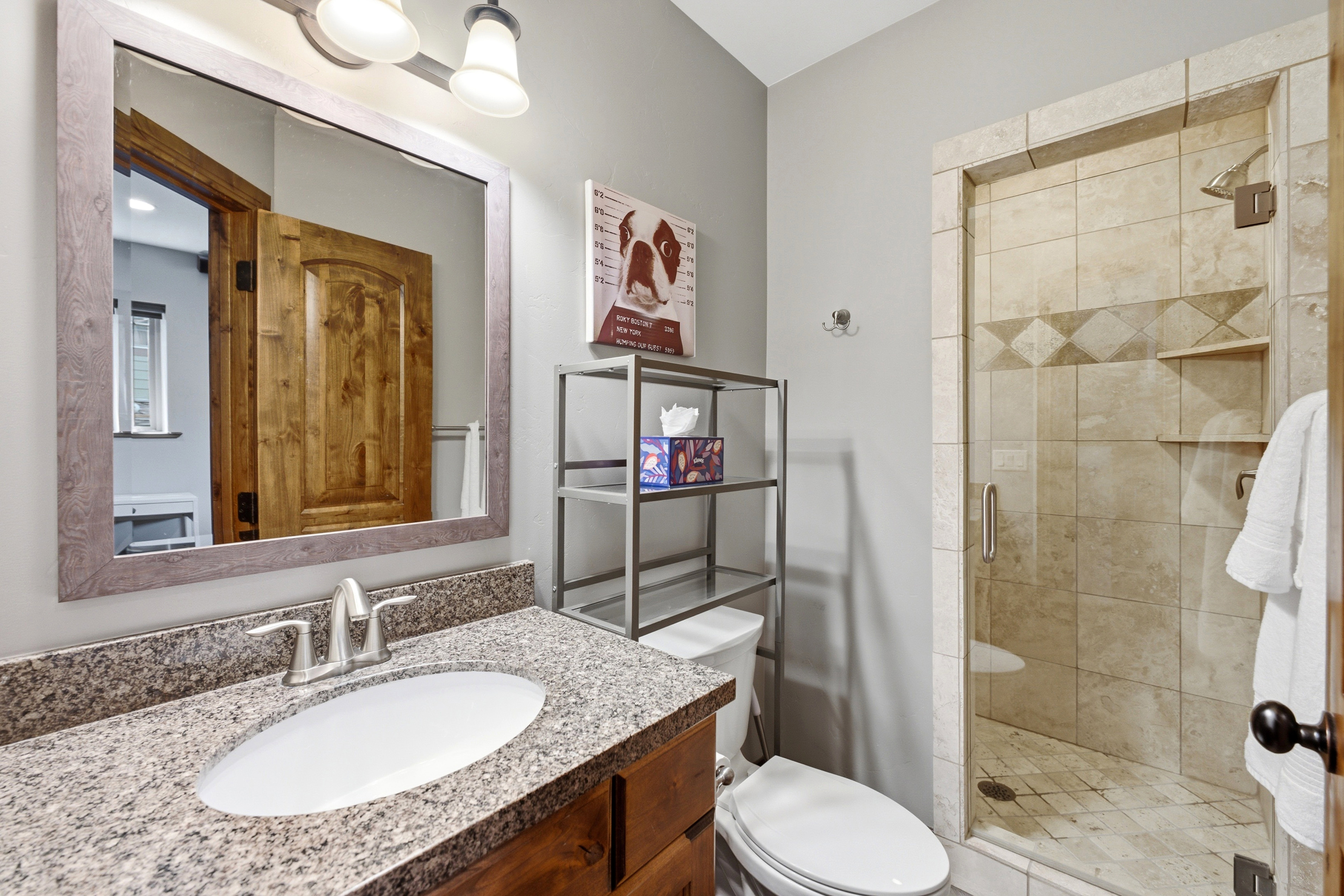 Bathroom featuring a wood-finish vanity with granite countertop, an undermount sink, and a framed mirror