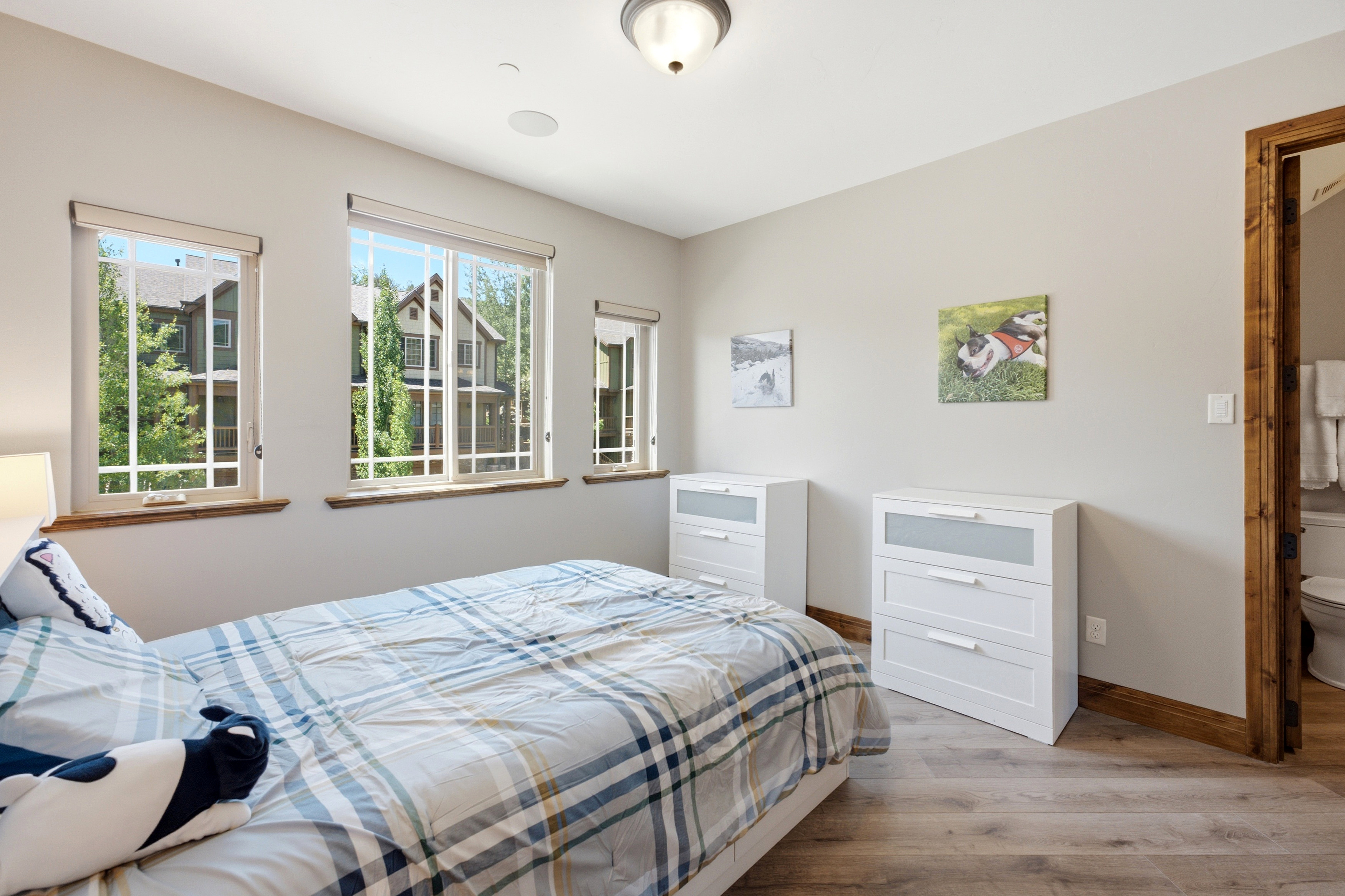 Room featuring wood-finish flooring, three windows with wood sills, light gray wall paint, and a wood-trimmed doorway