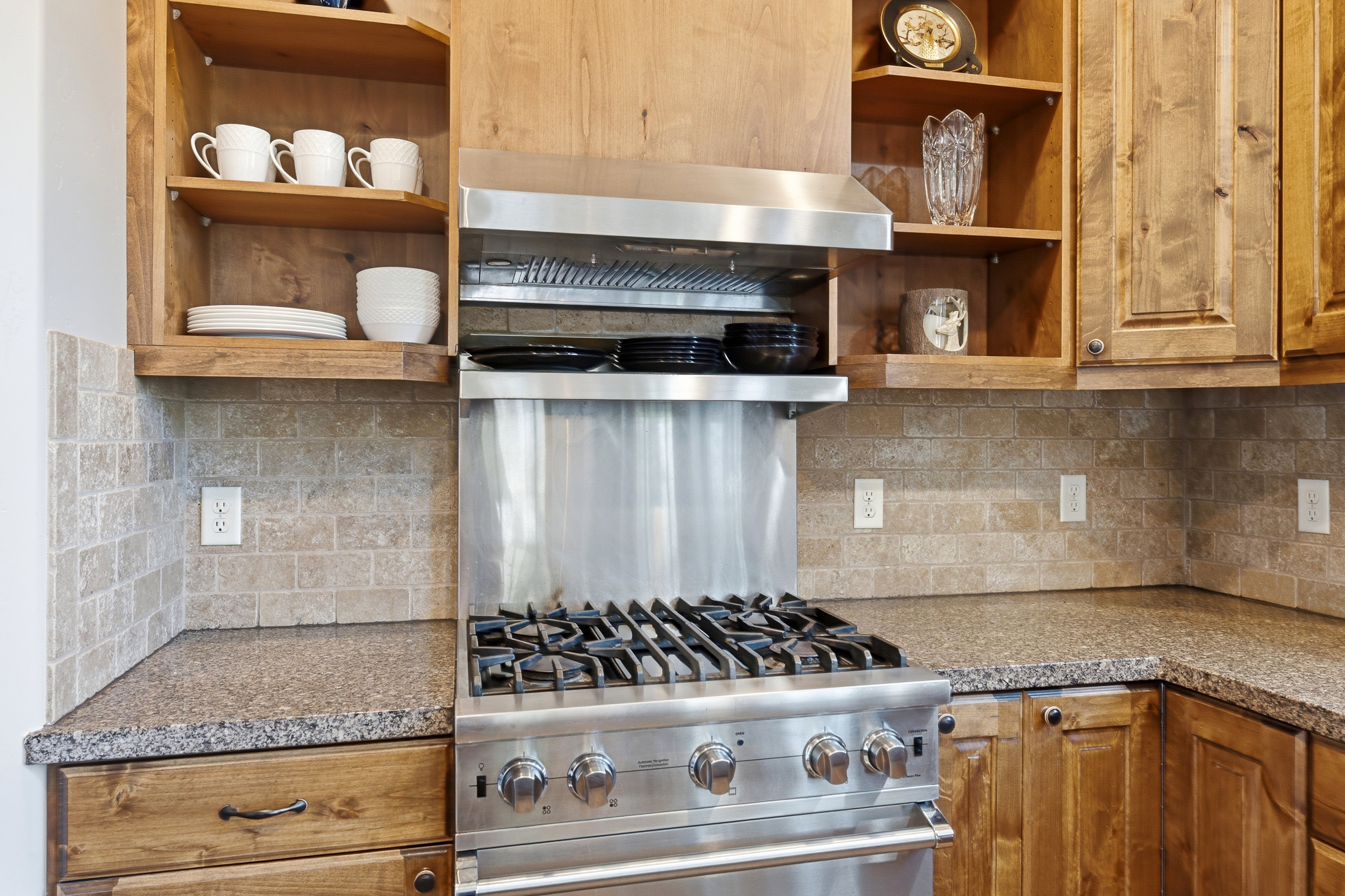 Gourmet kitchen featuring a stainless steel gas range, coordinating range hood, granite countertops, and a stone tile backsplash