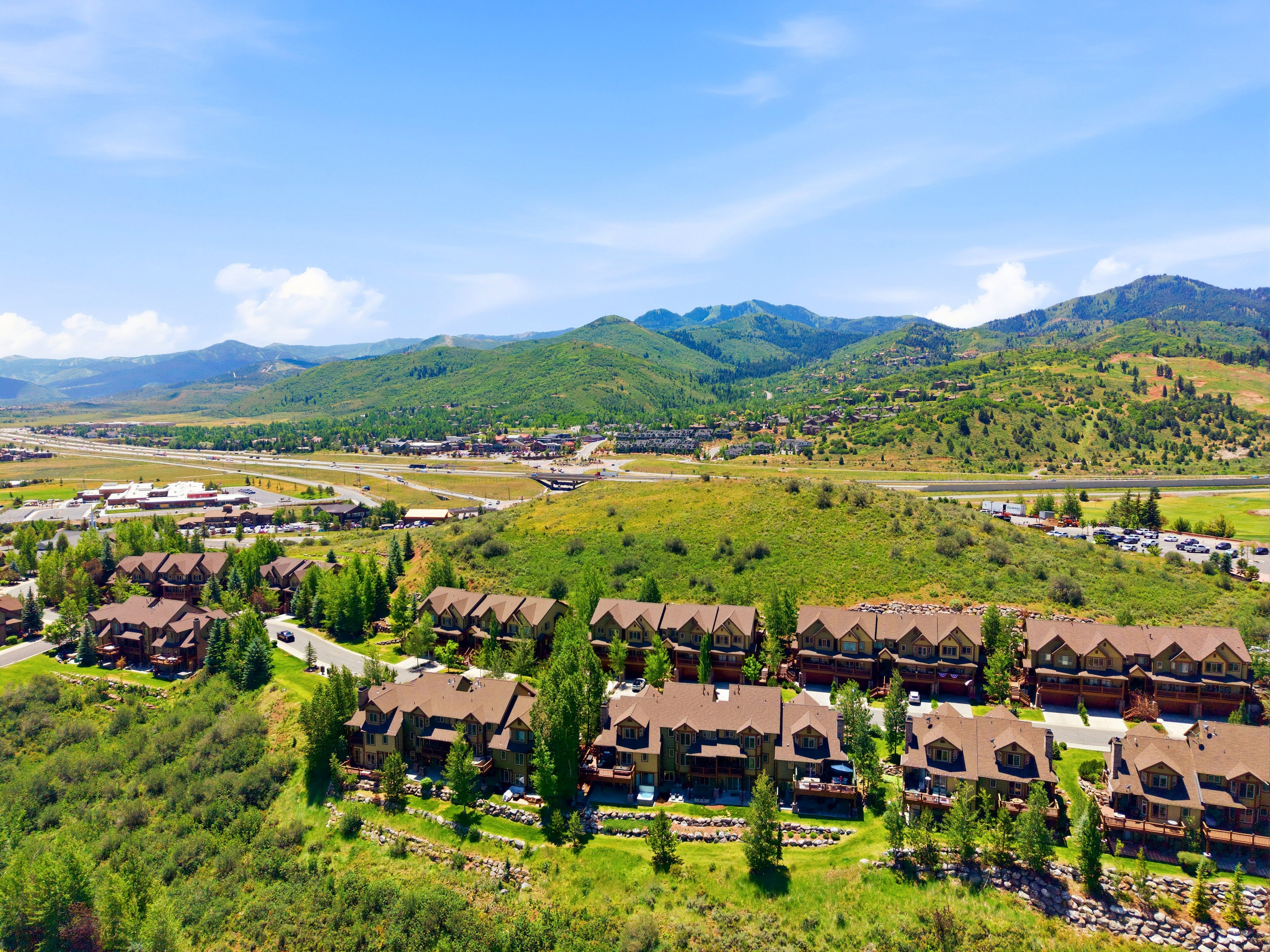 Expansive mountain landscape featuring multiple multi-story residences with brown roofs and exterior siding, surrounded by mature trees and lush green hillsides