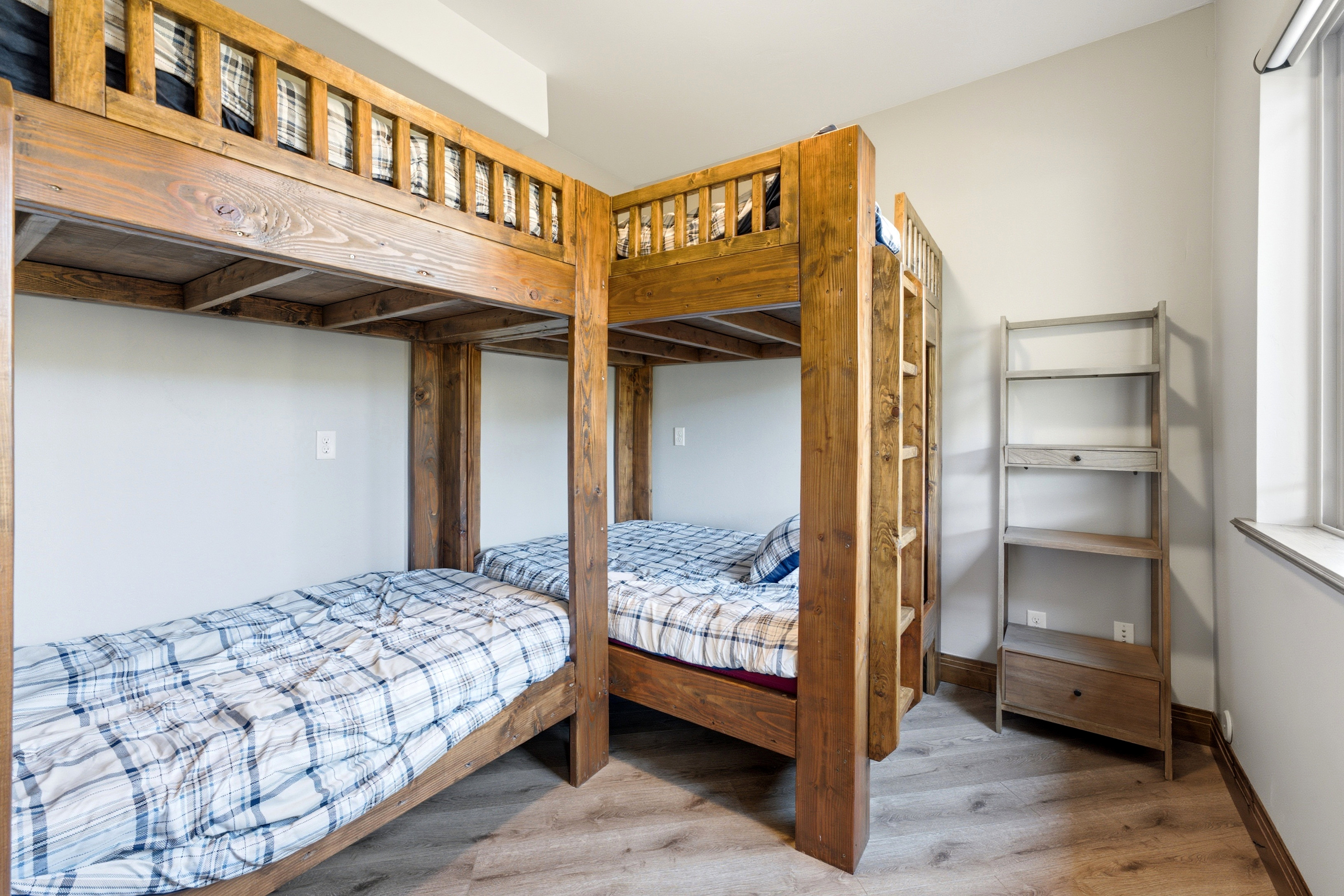 Integrated wooden bunk beds with built-in ladders, wood-finish flooring, and a window with natural light
