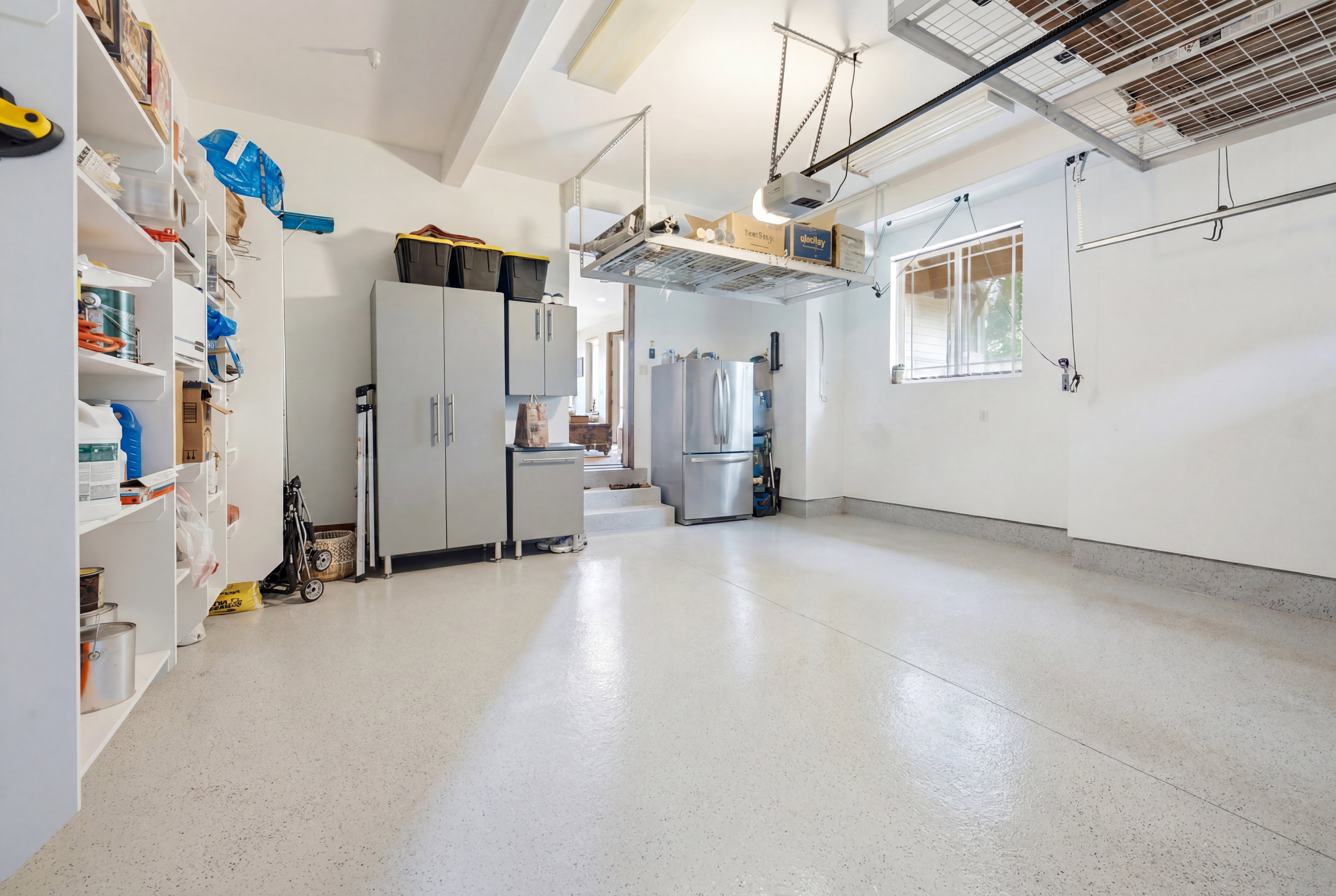 Garage with light-colored epoxy flooring, integrated shelving, built-in cabinetry, and overhead storage racks