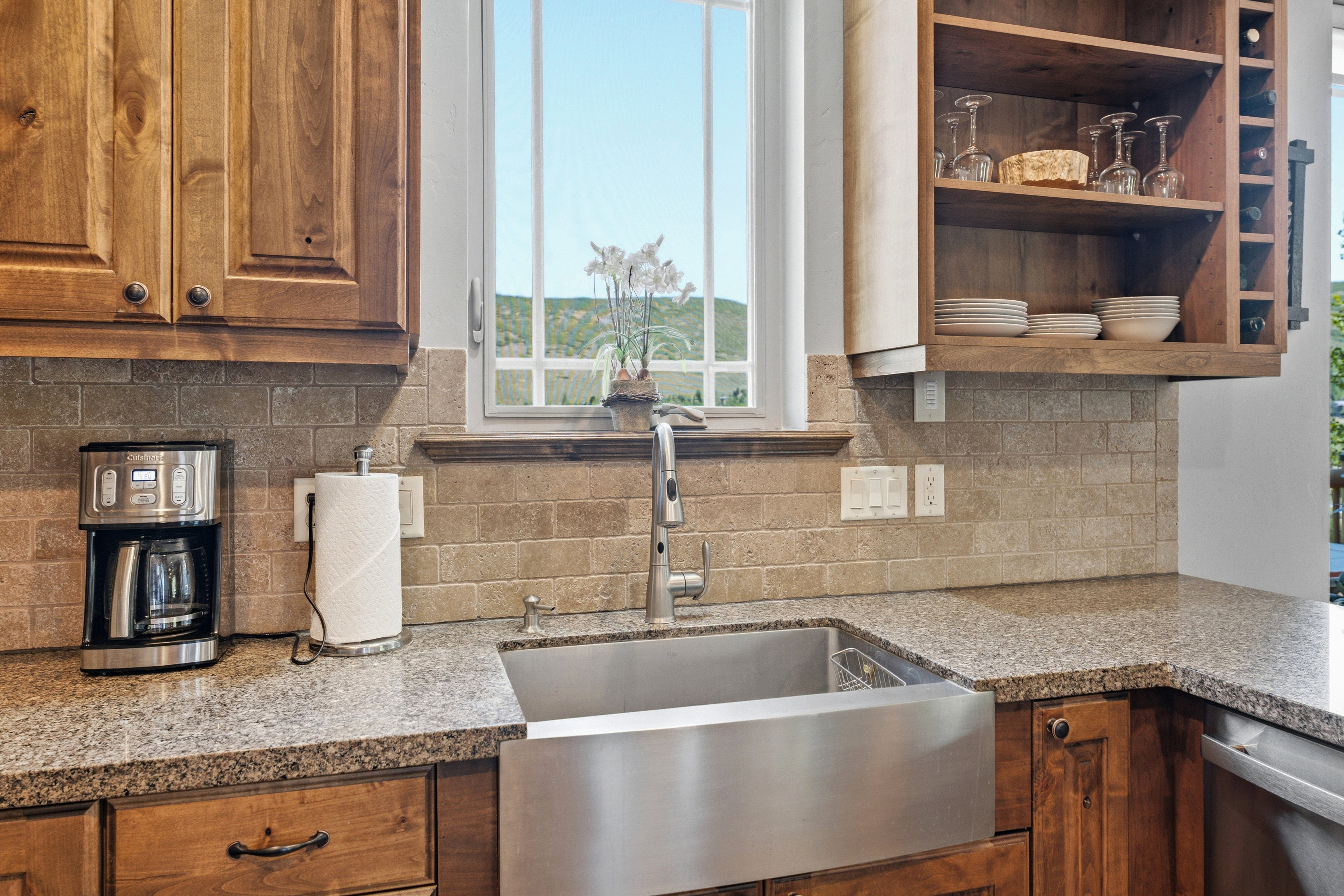 Kitchen featuring granite-look countertops, a stainless steel farmhouse sink with a gooseneck faucet, light brown subway tile backsplash, and wood-finish cabinetry