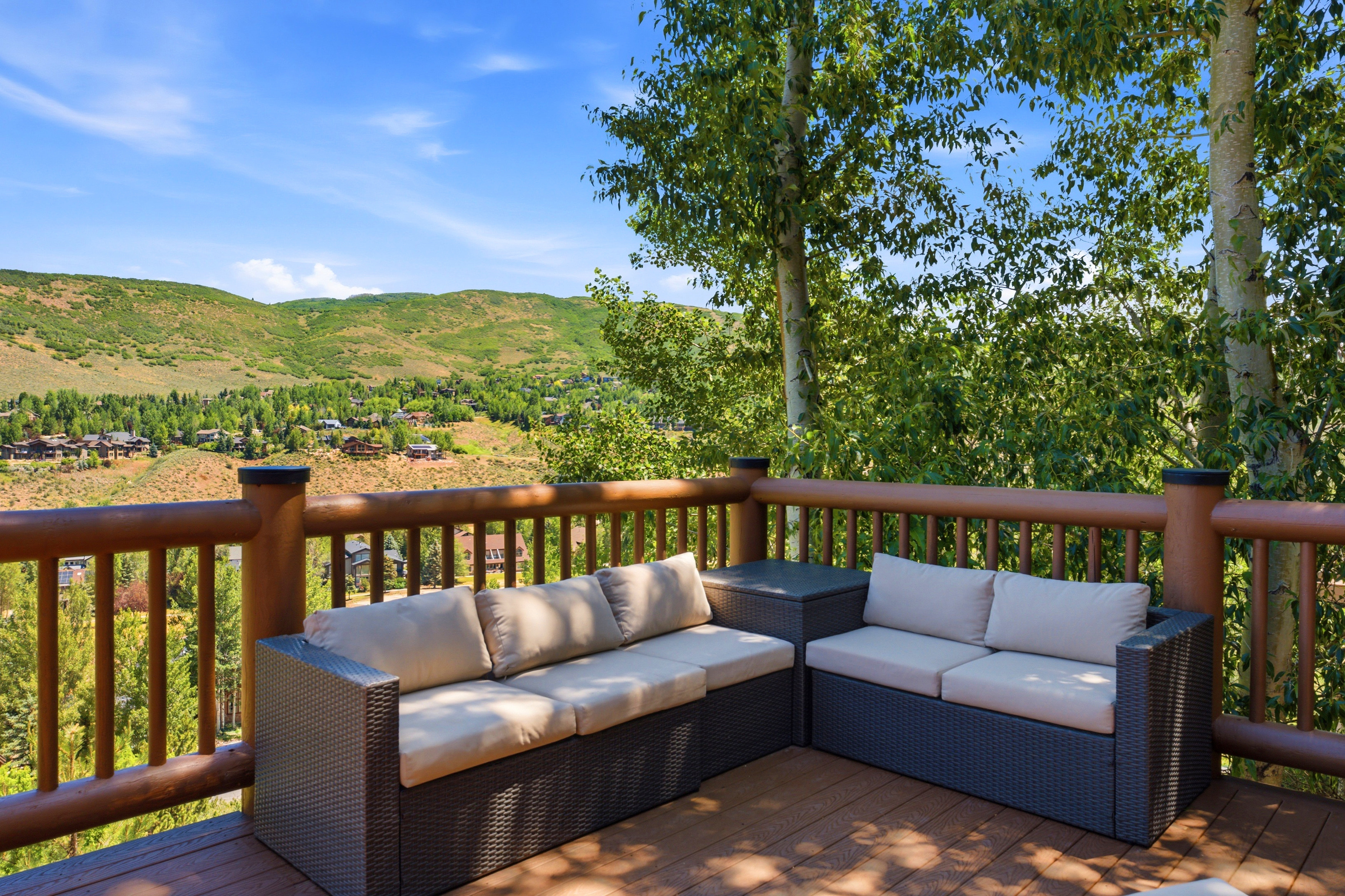 Spacious outdoor deck with mountain scenery, featuring a robust wood railing, composite decking, and mature trees providing natural shade