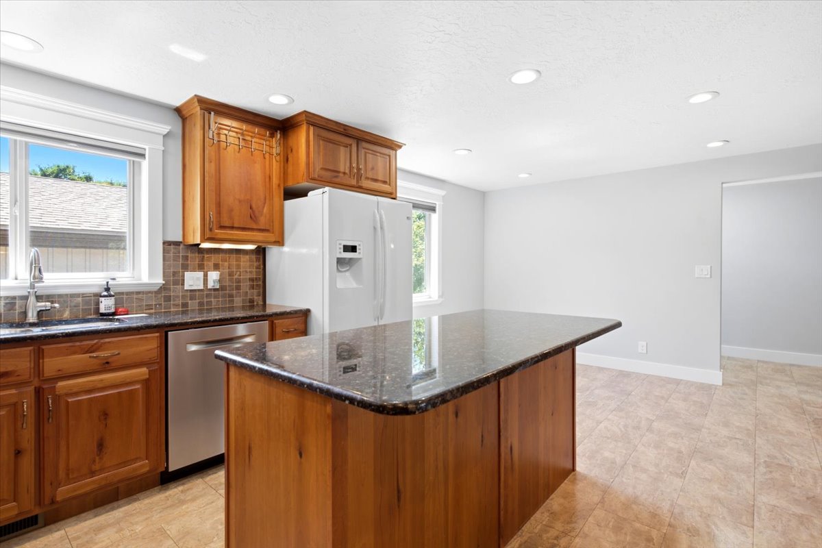 Kitchen featuring a central island with a dark countertop, wood cabinetry, stainless steel dishwasher, tile flooring, and recessed lighting