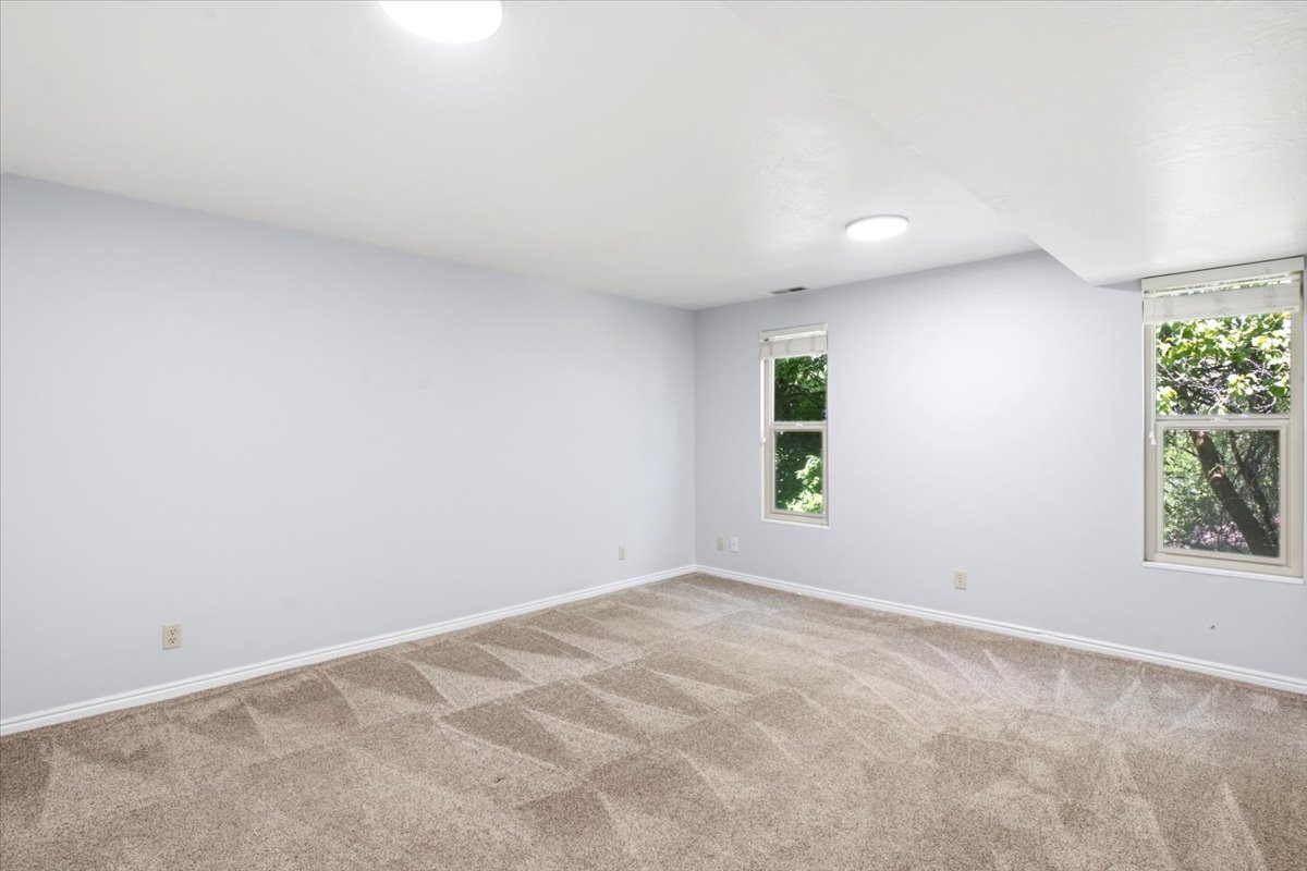 Spacious room featuring neutral carpeting, light blue walls, white trim, recessed lighting, and two windows with roller shades