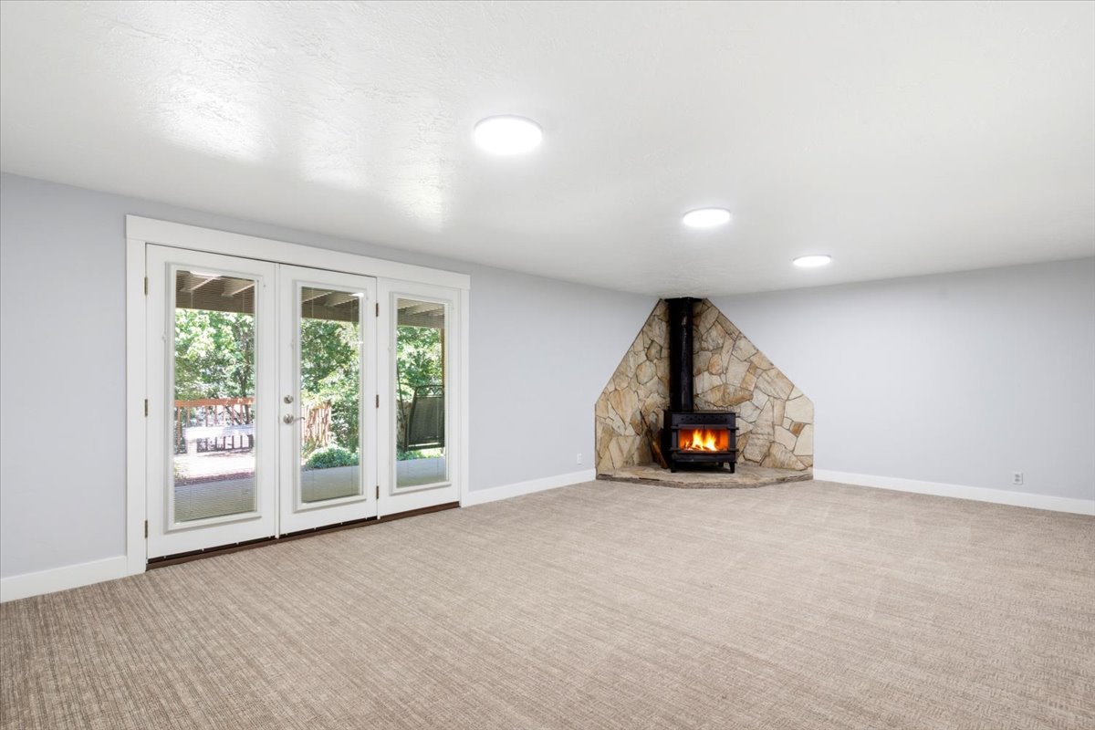 Spacious room featuring a stone-clad wood-burning stove, triple French doors, and recessed ceiling lighting