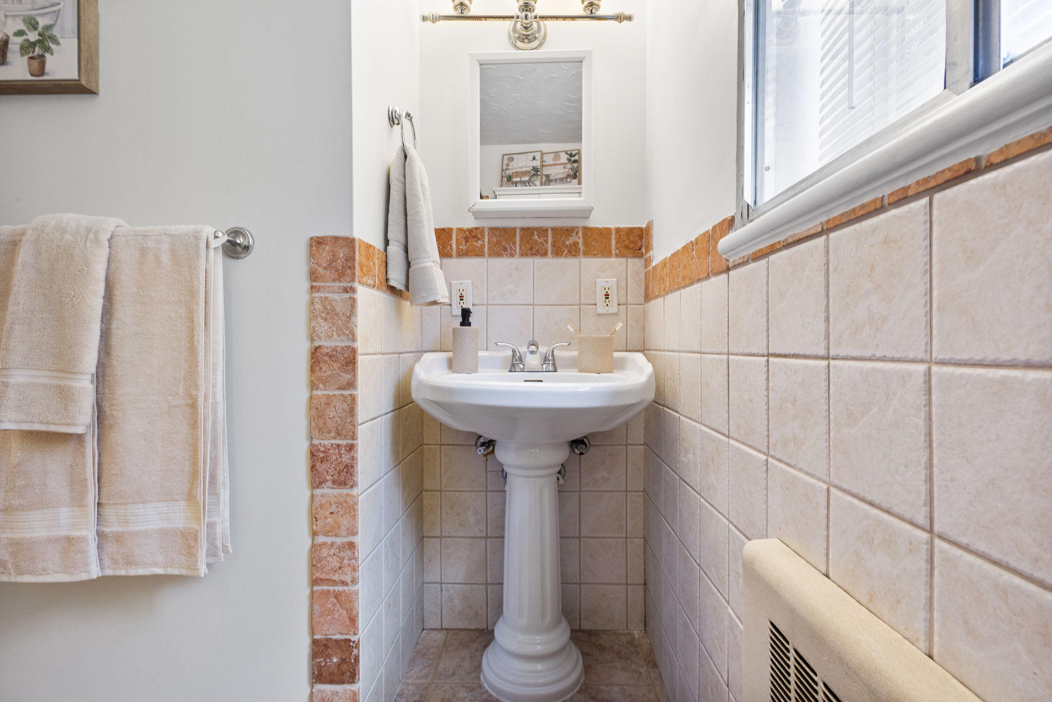 Pedestal sink with chrome fixtures, framed mirror, and a three-light vanity bar