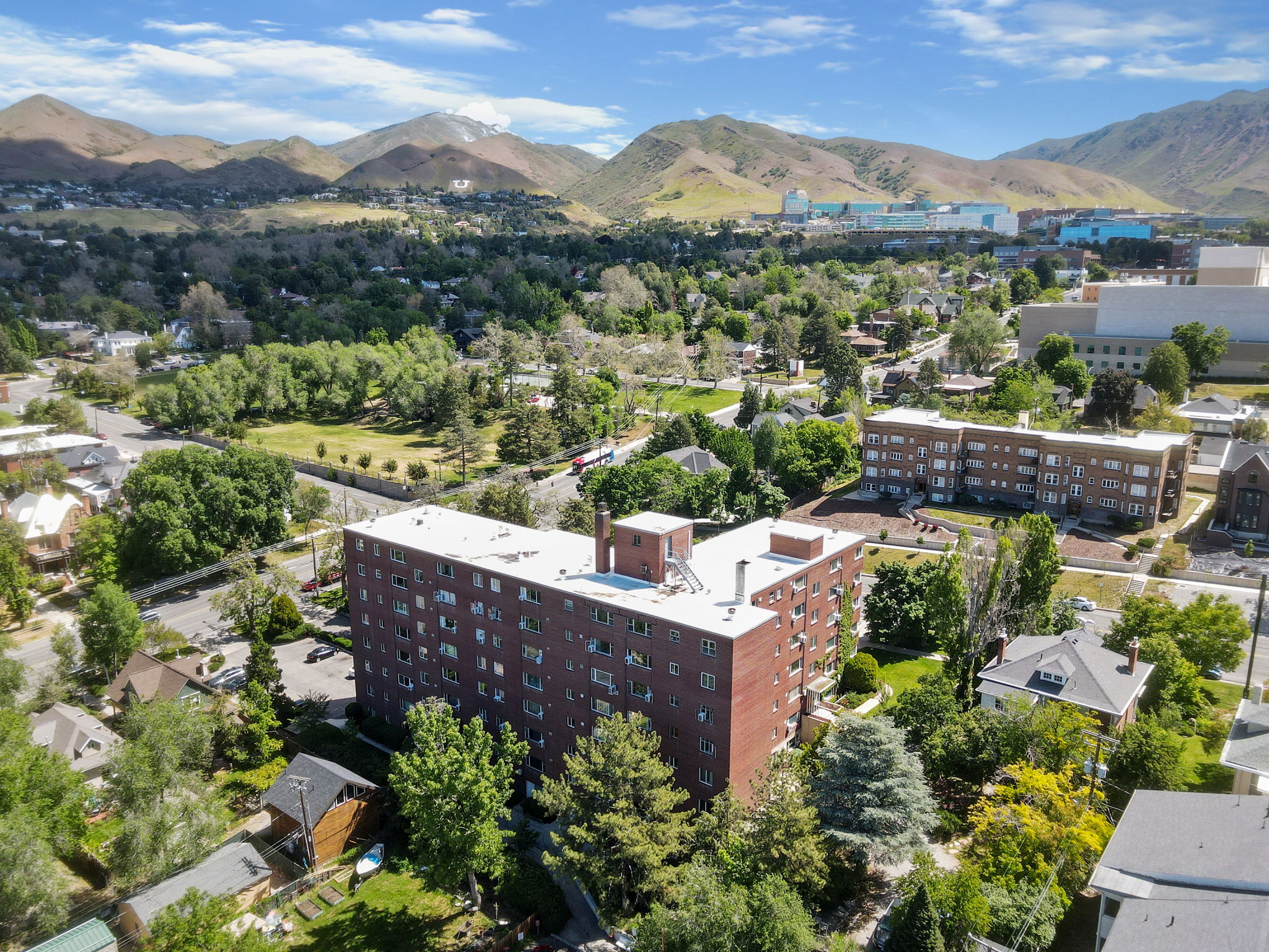 Multi-story brick building with multiple windows, surrounded by mature trees and paved areas