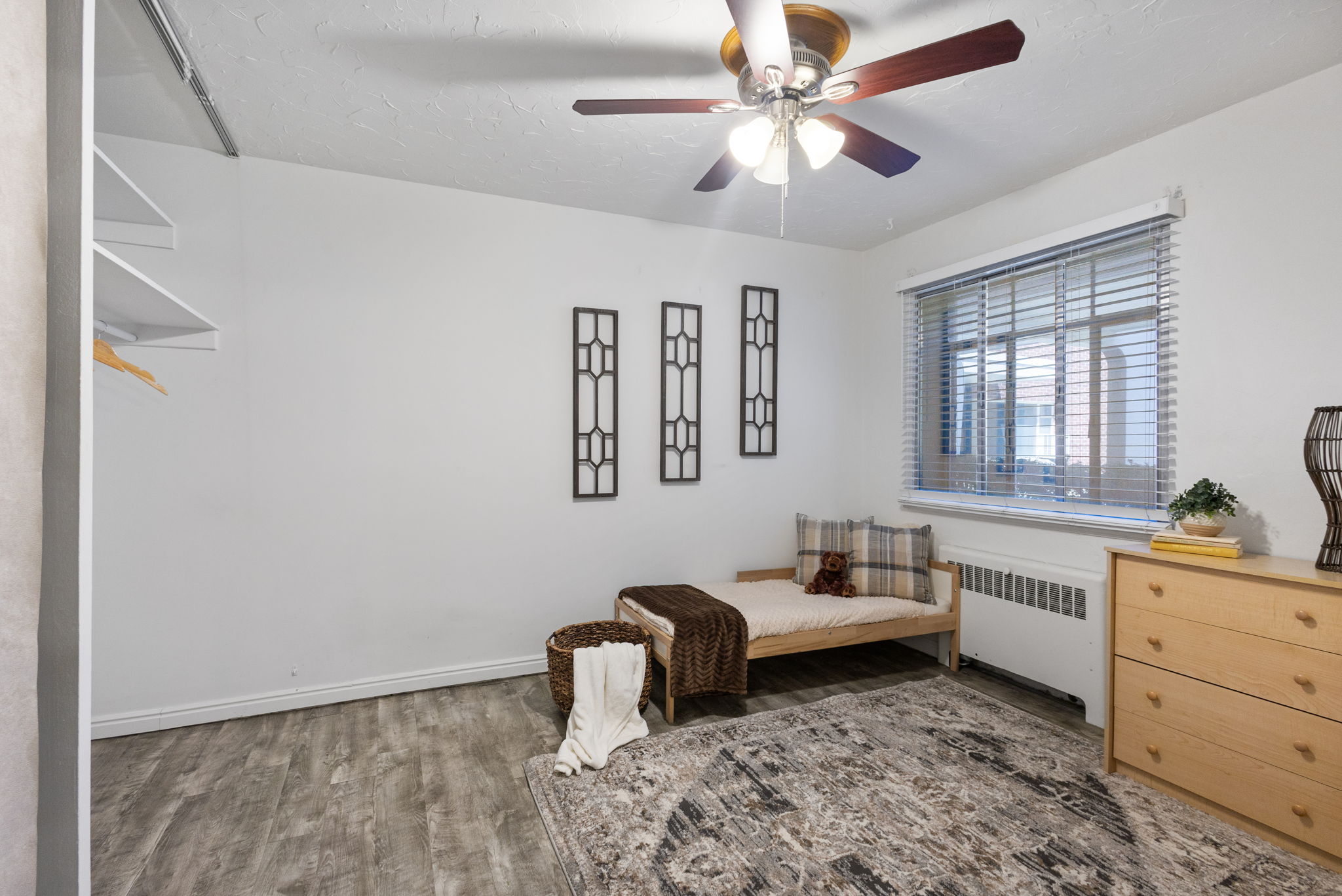 Second bedroom featuring a window with horizontal blinds, a ceiling fan with light fixture, and wood-finish flooring