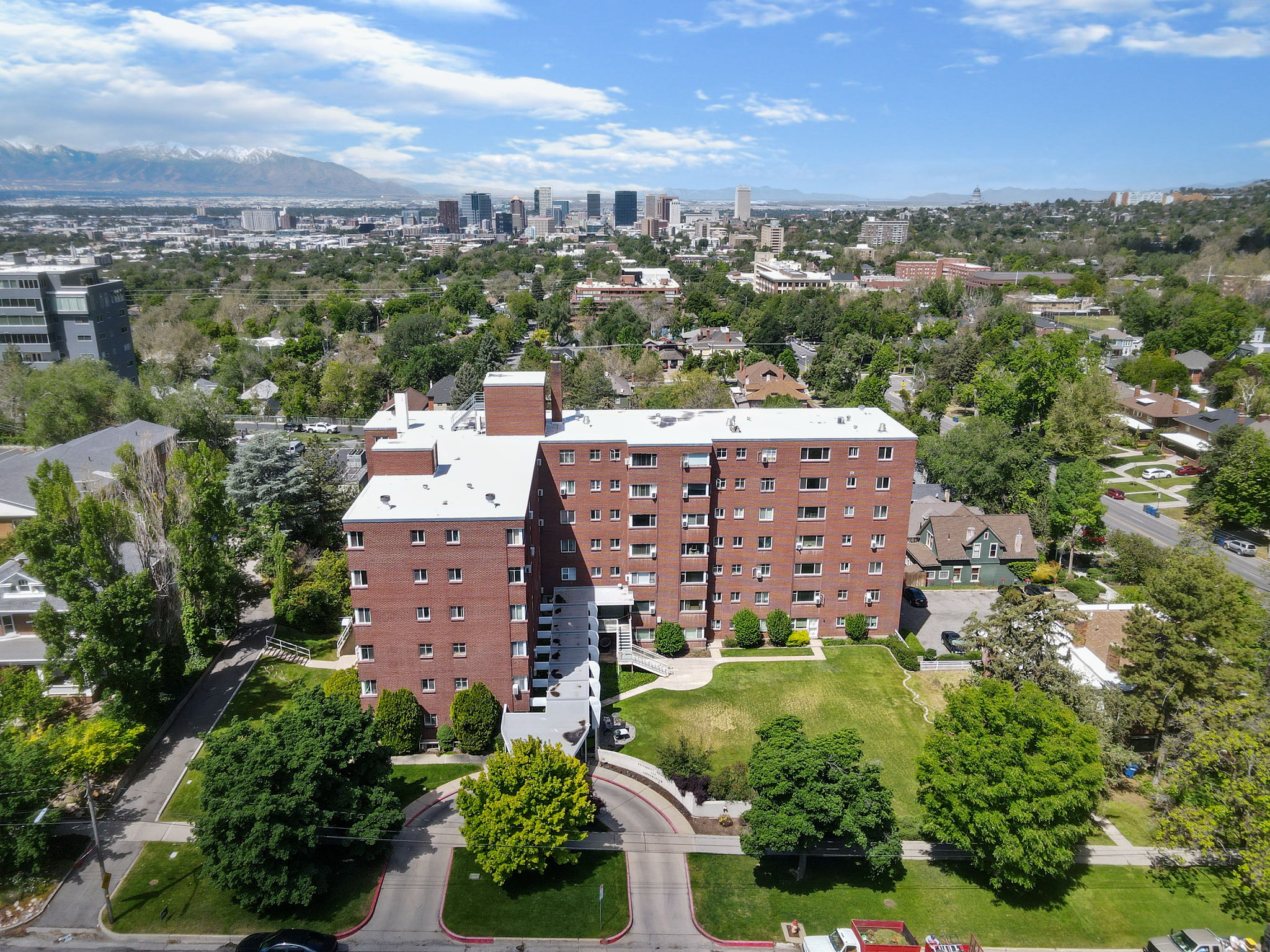 Multi-story brick building featuring a white roof, surrounding green landscaping, and mature trees