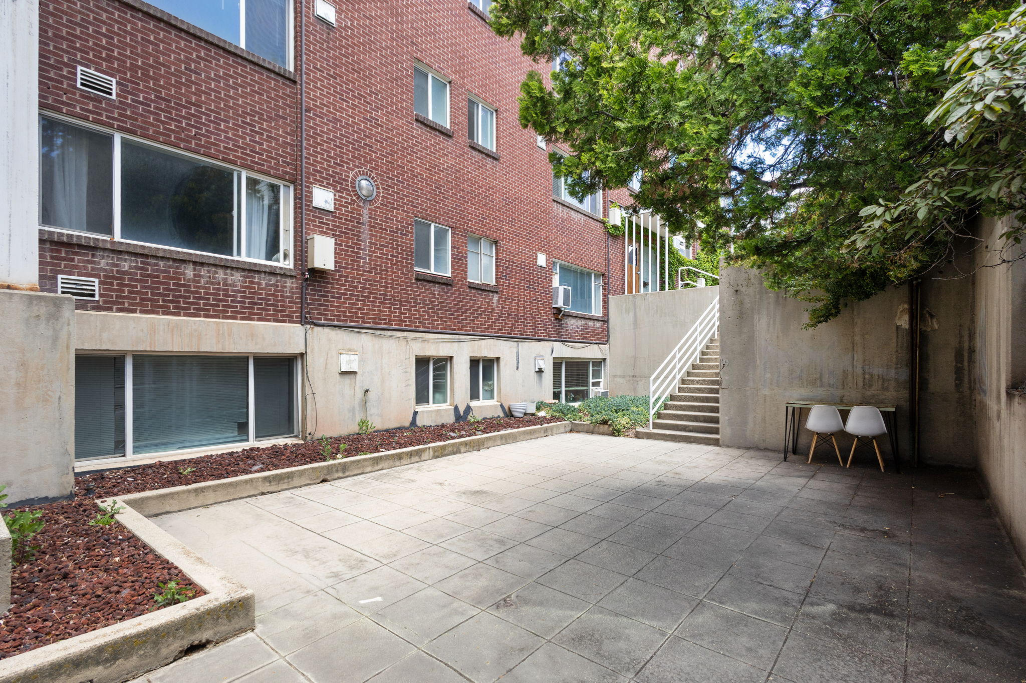 Expansive patio area featuring large concrete pavers, concrete retaining walls, and a brick exterior building