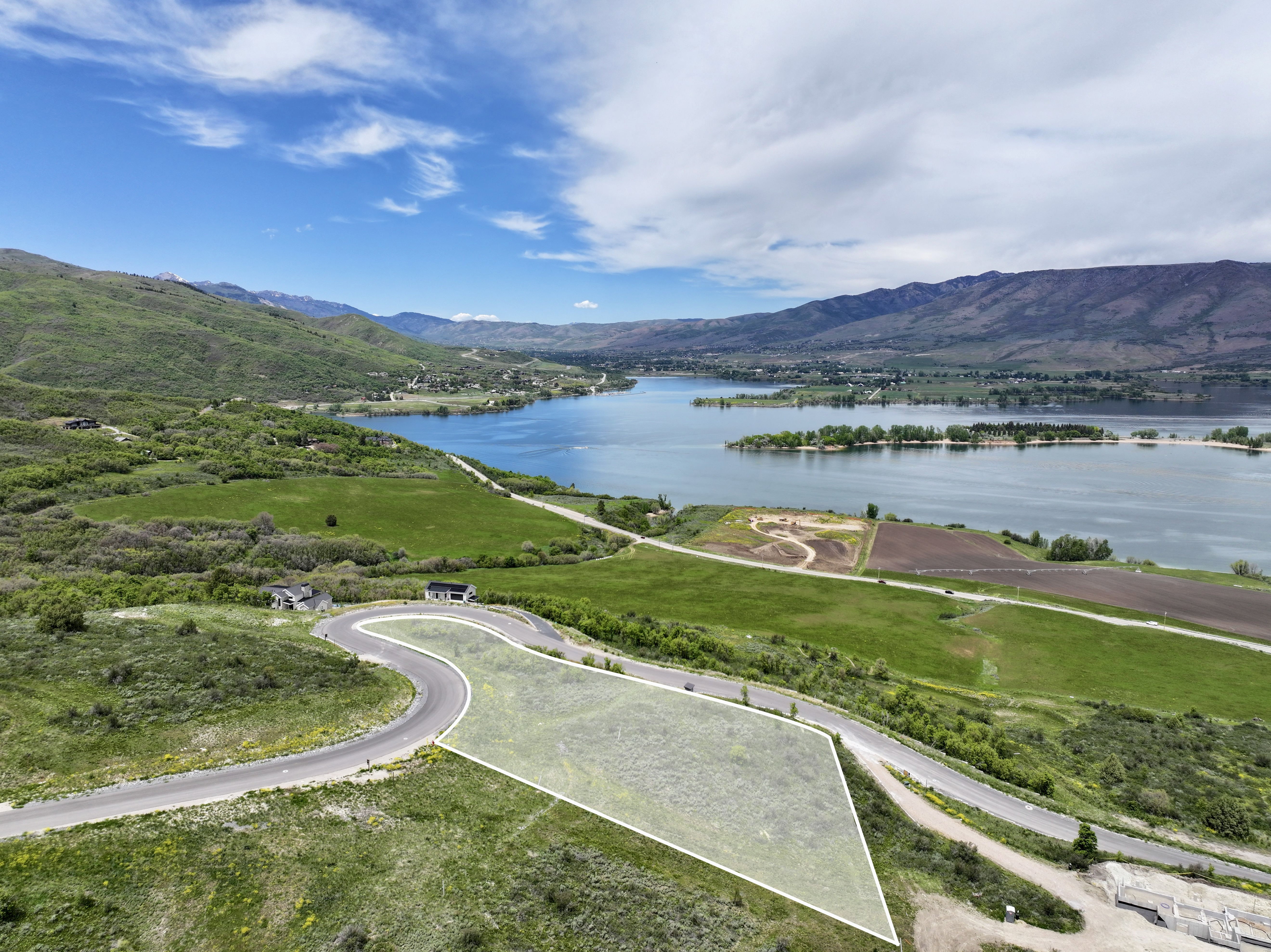Expansive lot with a marked boundary, featuring a curved paved road and lush green surroundings