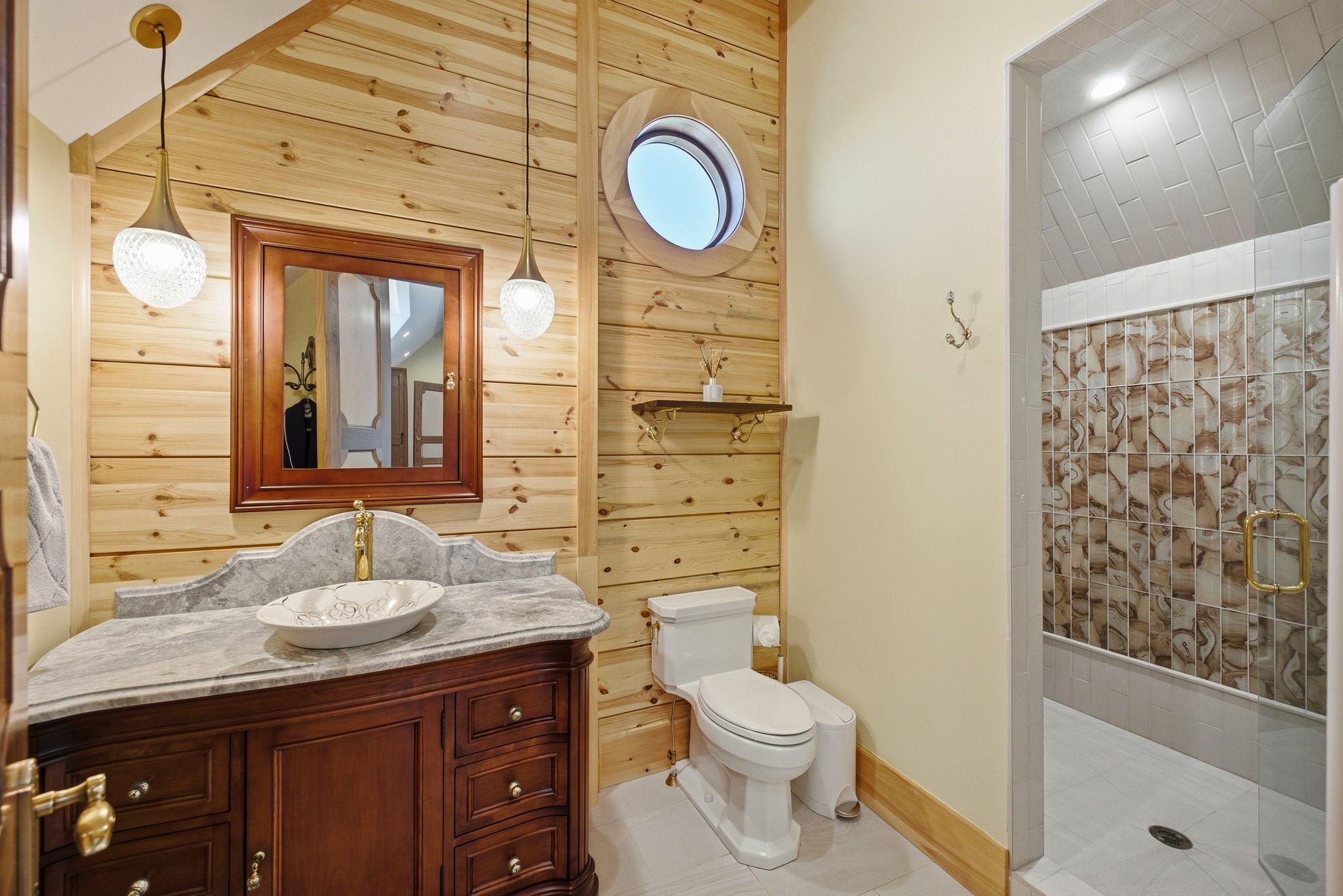 Bathroom with wood-paneled accent wall, a circular porthole window, and a shower enclosure