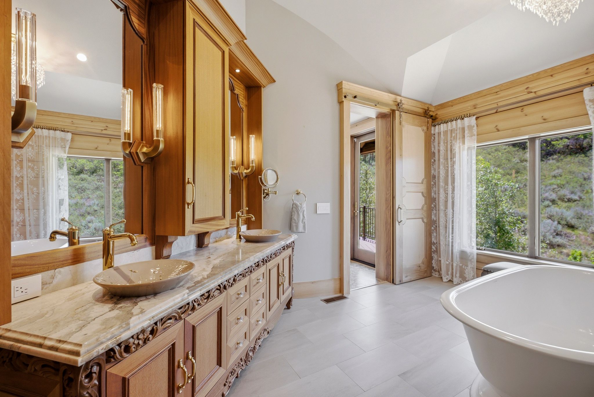 Spacious bathroom featuring a dual vanity with carved wood cabinetry, marble-finish countertop, and vessel sinks