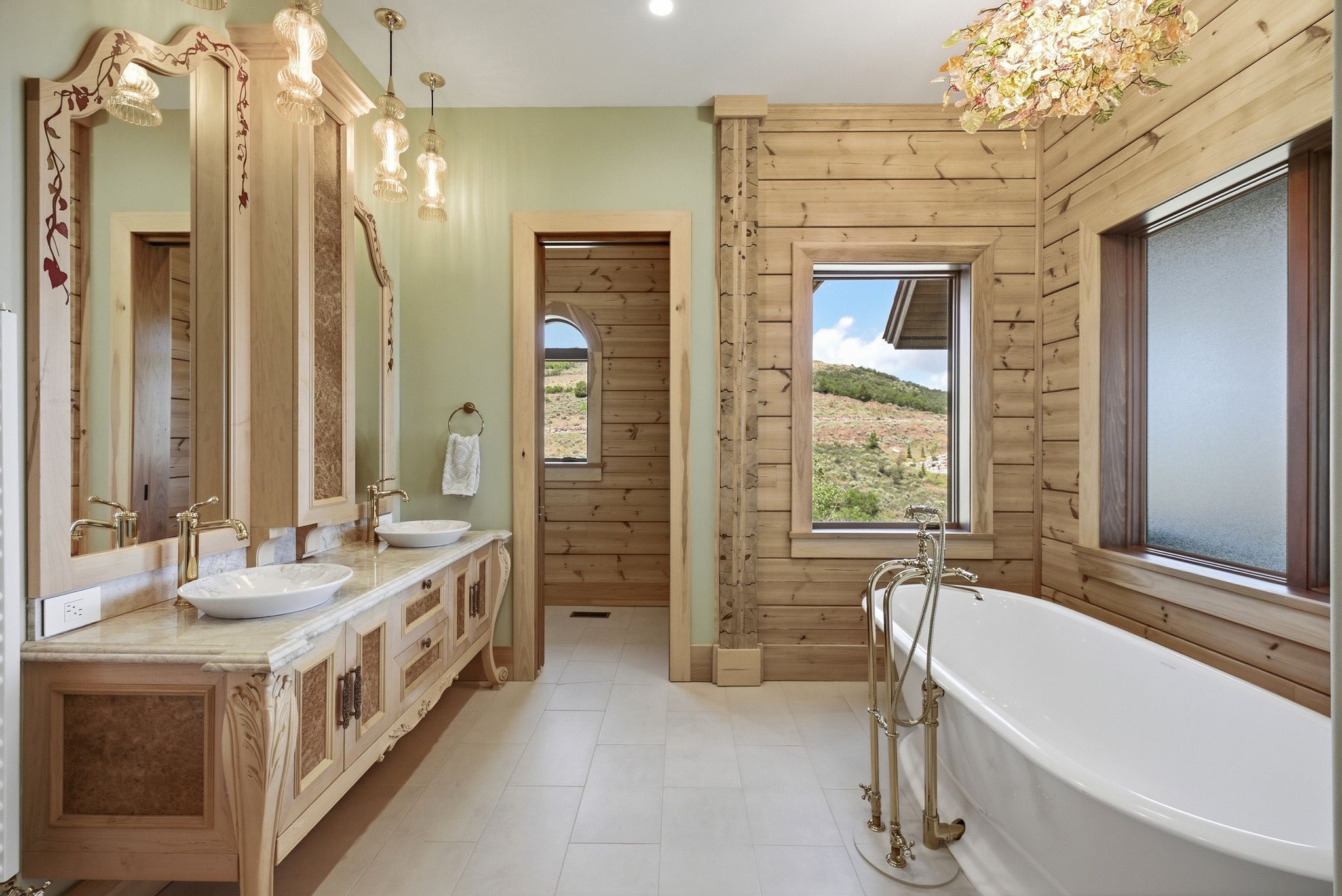 Bathroom featuring a freestanding soaking tub with floor-mounted fixtures, wood plank wall paneling, and a dual vanity with vessel sinks, ornate cabinetry, and pendant lighting