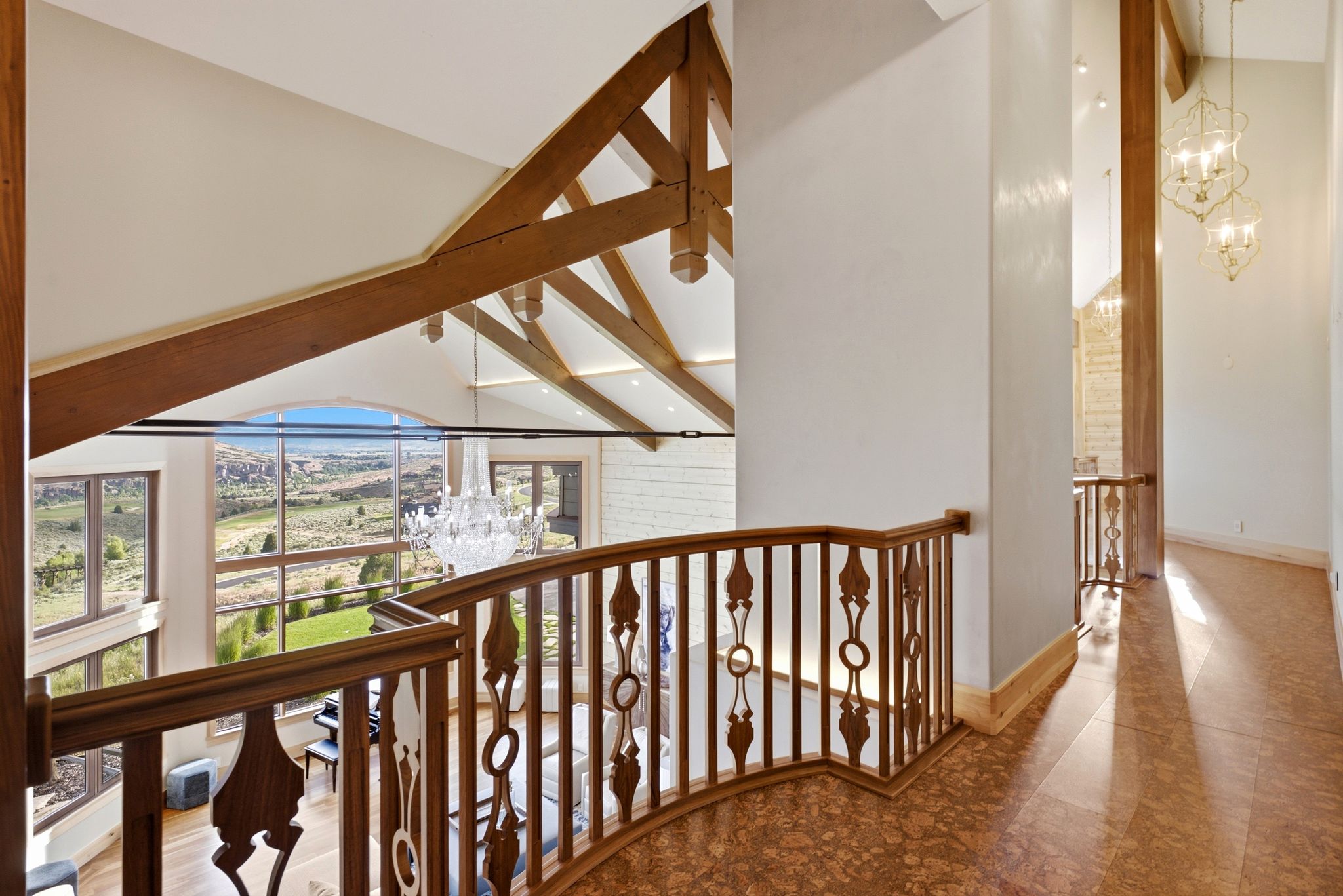 Upper-level hallway featuring ornate wood-finish railing, patterned flooring, and decorative hanging light fixtures