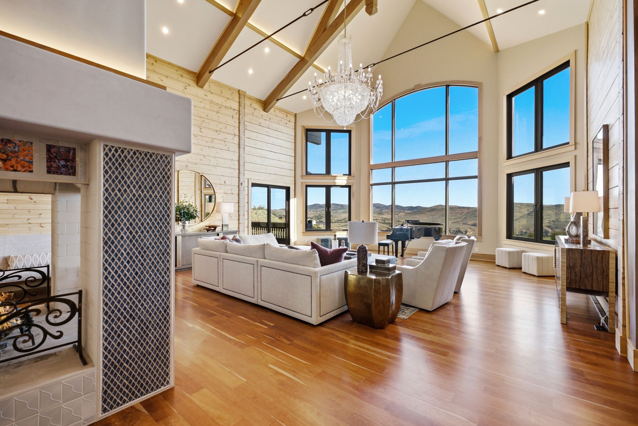 Grand living area featuring vaulted ceilings with exposed wood beams, a prominent crystal chandelier, and extensive floor-to-ceiling windows