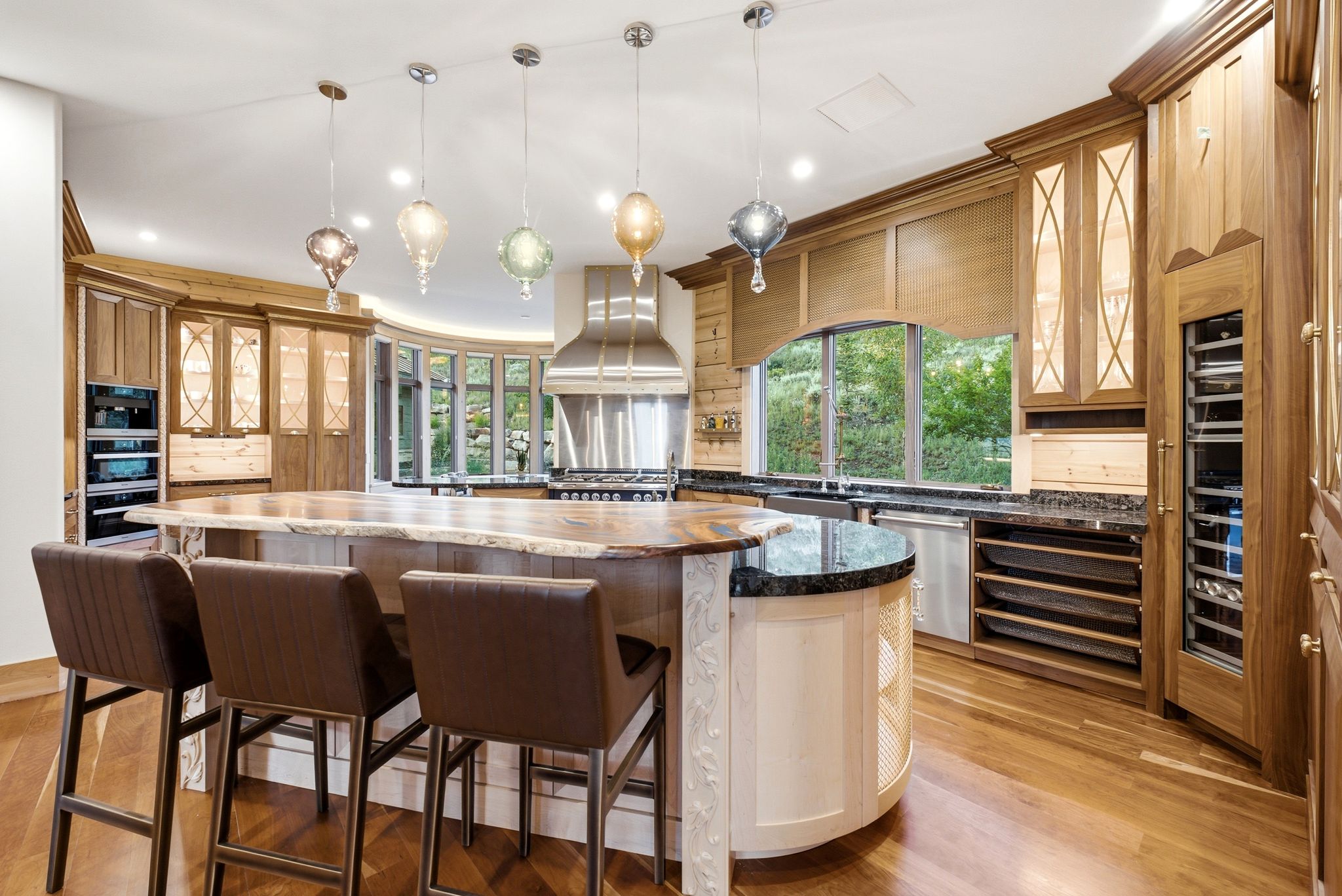 Gourmet kitchen featuring a live-edge island countertop, custom cabinetry with glass-front accents, stainless steel appliances, and a built-in wine cooler