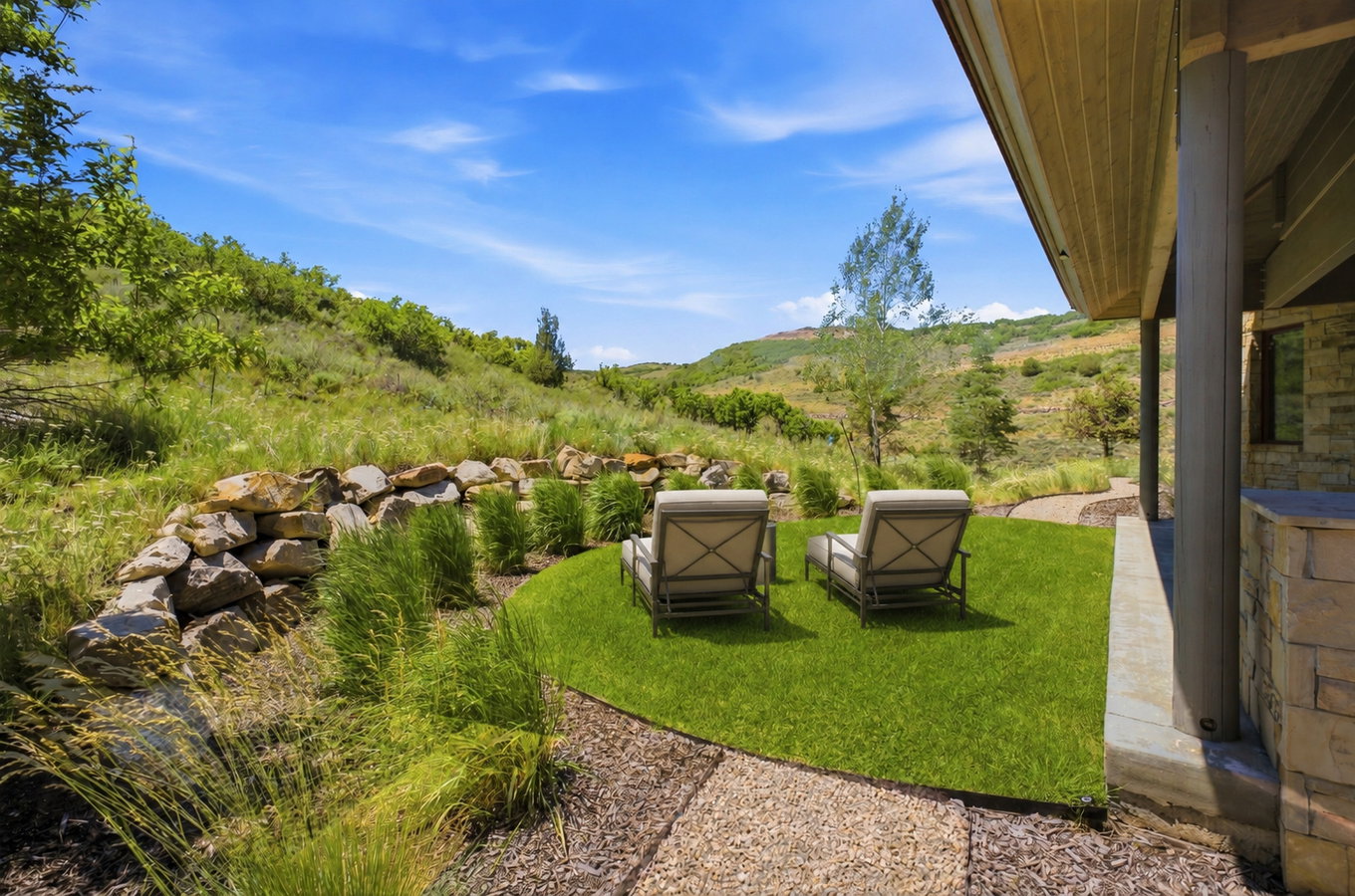 Terraced outdoor area featuring a manicured lawn, natural stone retaining wall, and verdant landscaping