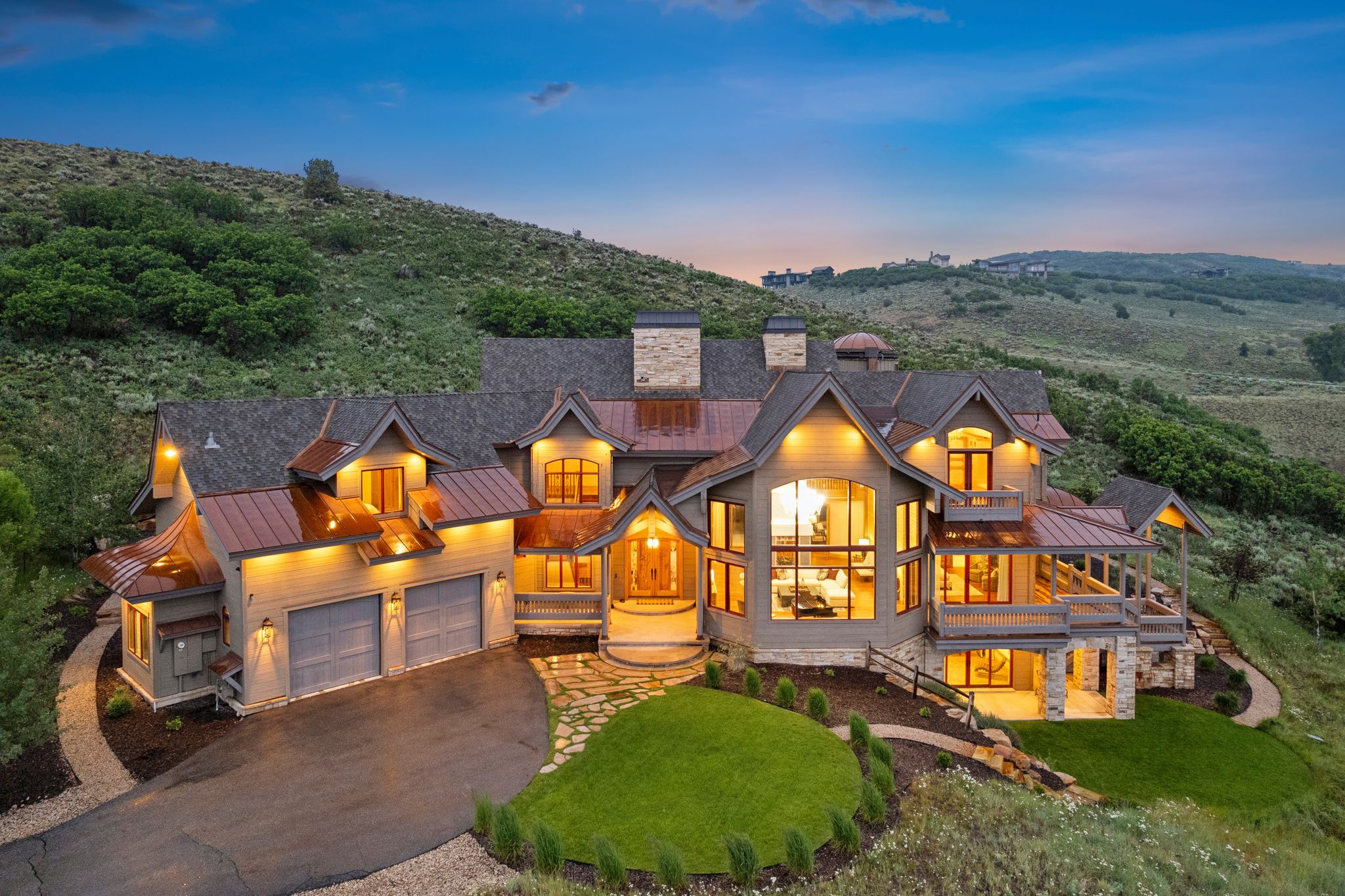 Custom-built residence featuring copper roofing details, stone accents, multiple balconies, a paver driveway, and an attached two-car garage