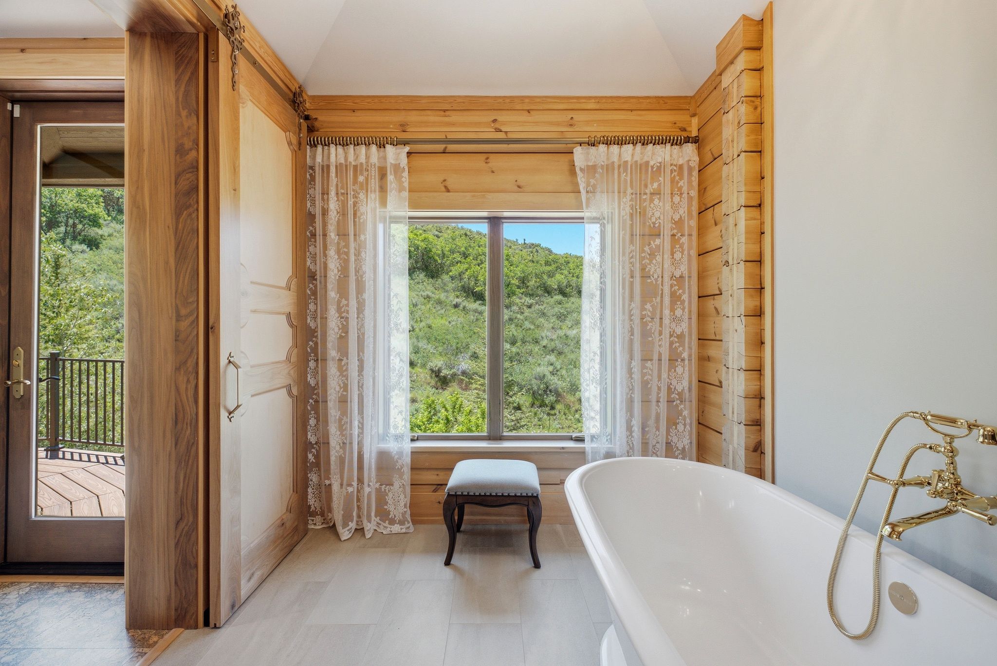 Freestanding soaking tub with brass fixtures, set against a window with outdoor scenery