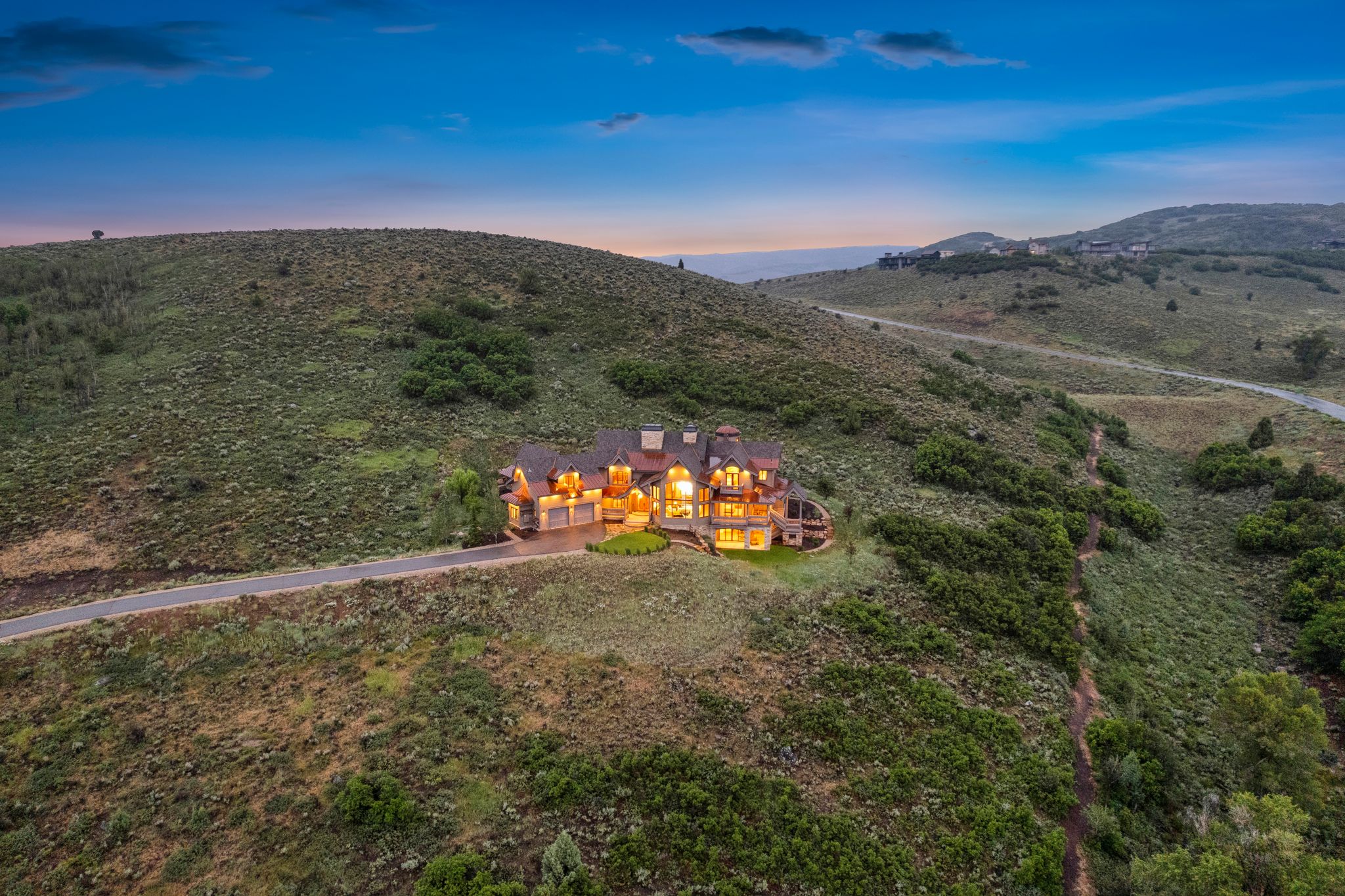 Hillside property featuring a stone and stucco exterior, multiple gables, and illuminated windows