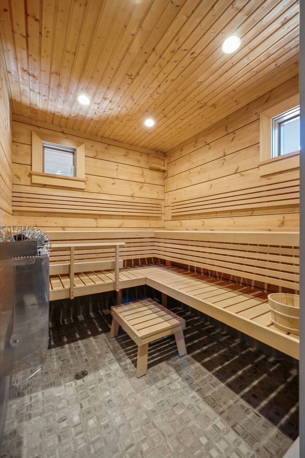 Dedicated sauna featuring light wood paneling, multi-level slatted benches, and a mosaic tile floor