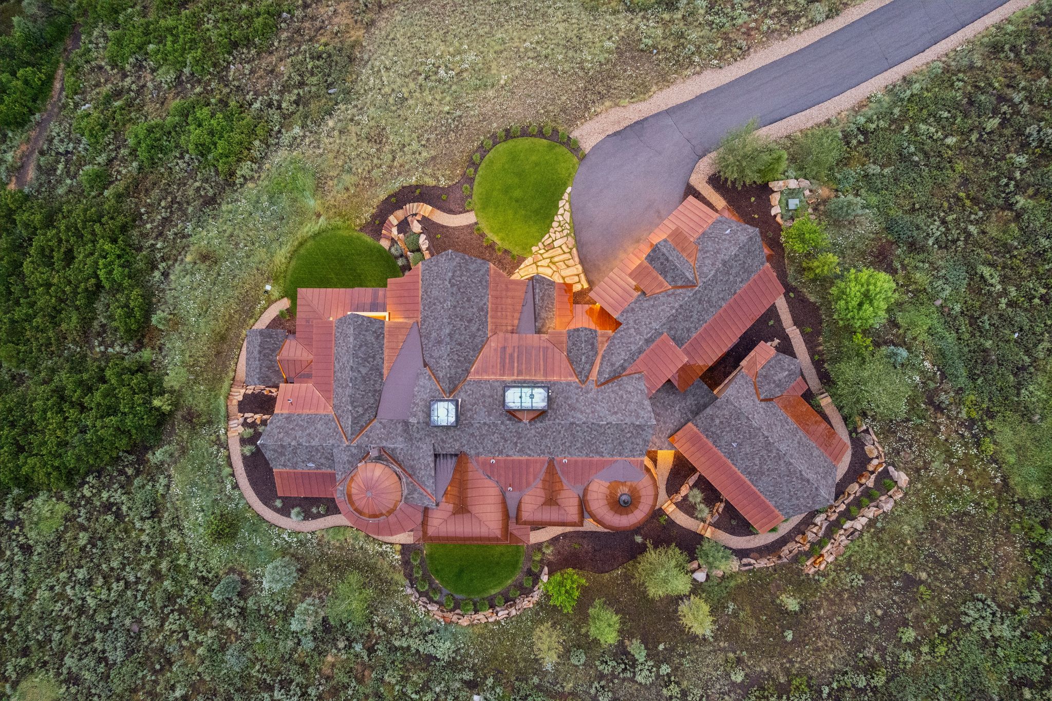 Expansive property featuring a multi-gabled shingle roof, a circular driveway, and a terraced landscape with manicured lawns