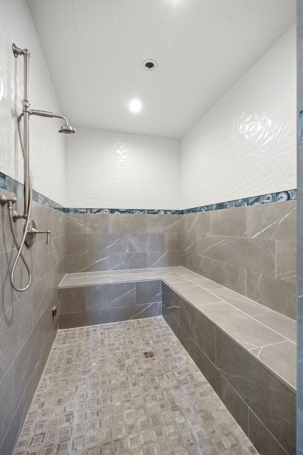Spacious tiled shower featuring a built-in bench, rainfall showerhead, handheld shower fixture, and recessed lighting