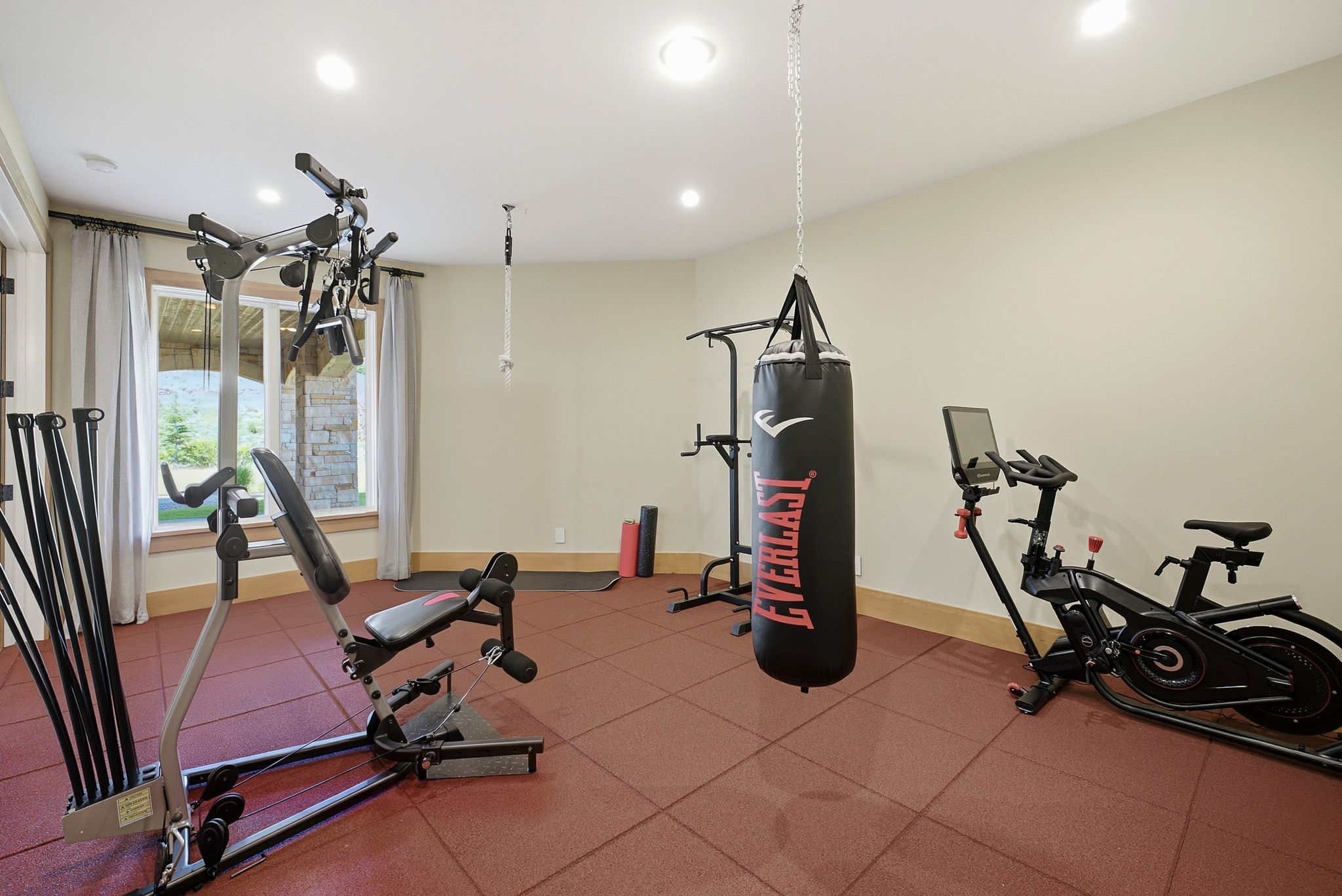 Dedicated fitness room featuring red interlocking floor tiles, recessed lighting, and a large window with drapes