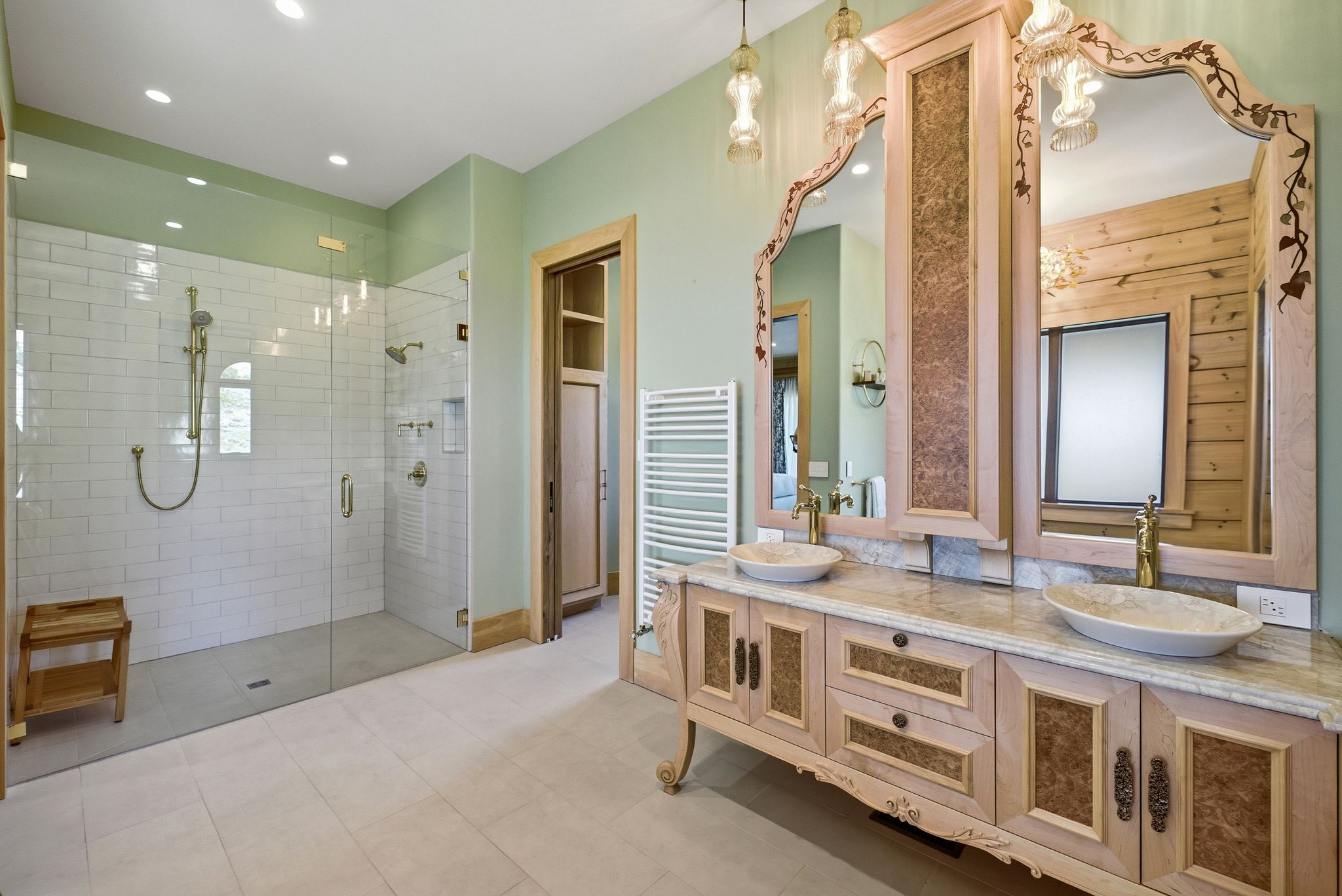 Spacious bathroom featuring a frameless glass shower with subway tile, a dual vanity with vessel sinks, ornate mirrors, and light-toned flooring