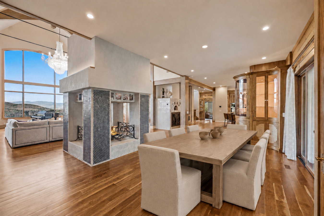 Open-concept living space featuring wood-finish flooring, a multi-sided fireplace with tile accents, and extensive windows