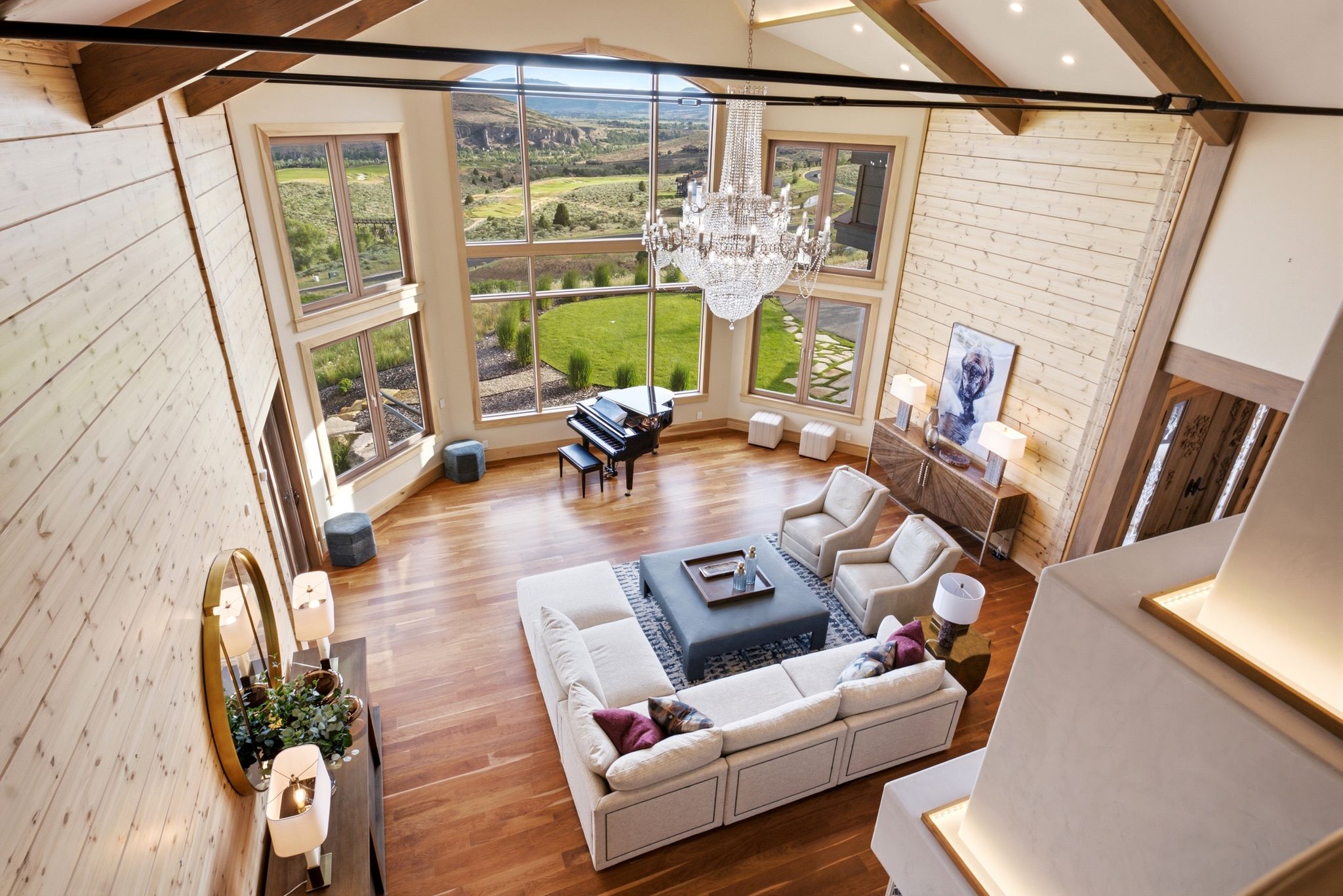 Open-concept living area featuring a vaulted ceiling with exposed wood beams, expansive floor-to-ceiling windows, and hardwood flooring