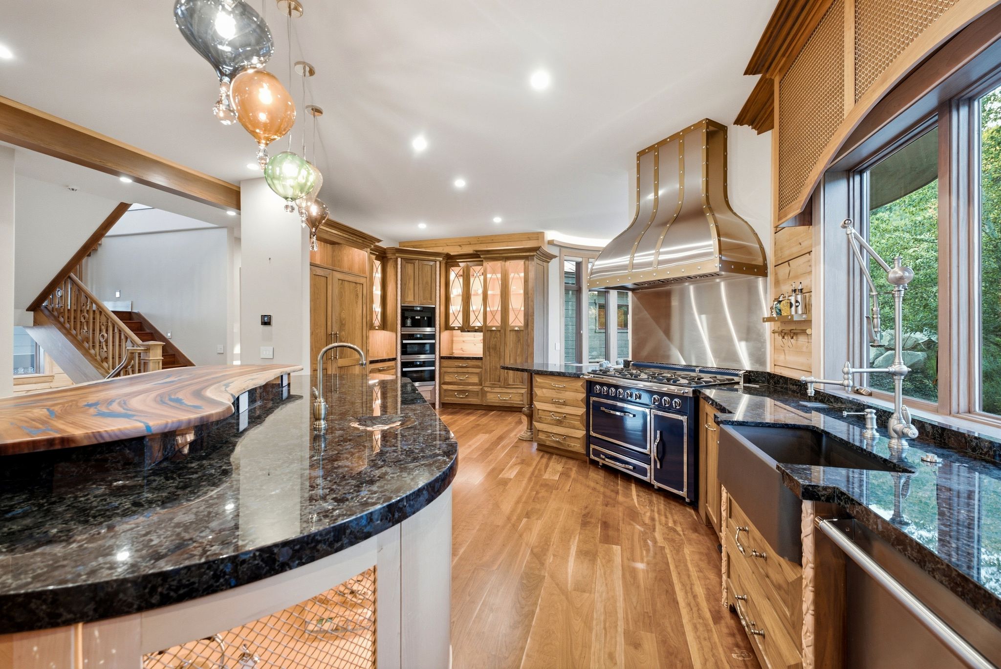 Gourmet kitchen with wood-finish flooring, dark granite countertops, stainless steel appliances, and custom wood cabinetry