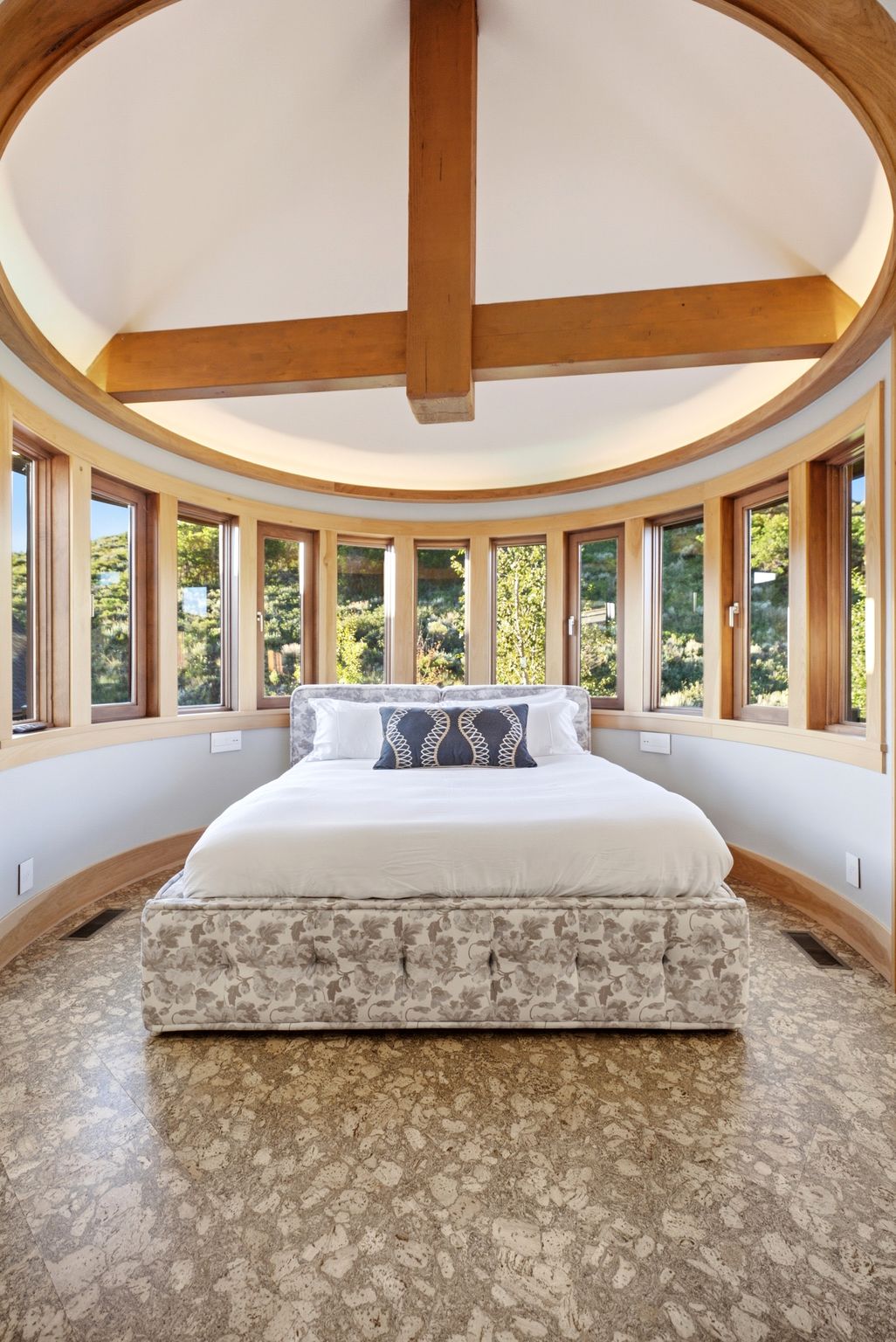 Curved wall with a continuous band of wood-framed windows, exposed timber ceiling beams, and a light-toned patterned floor